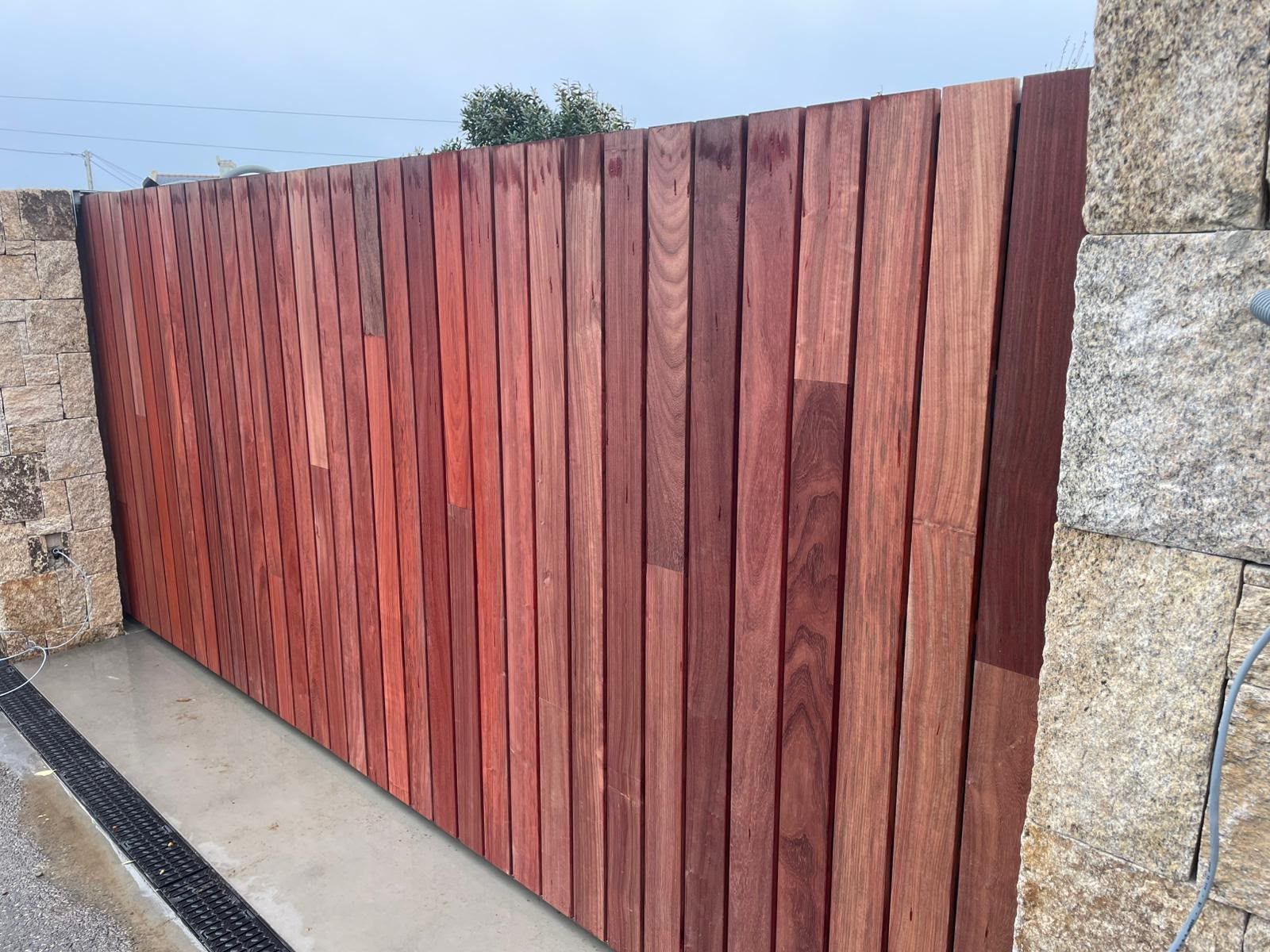 Portail d’allée en lattes de bois entre des murs en pierre, avec des planches verticales brun rougeâtre.