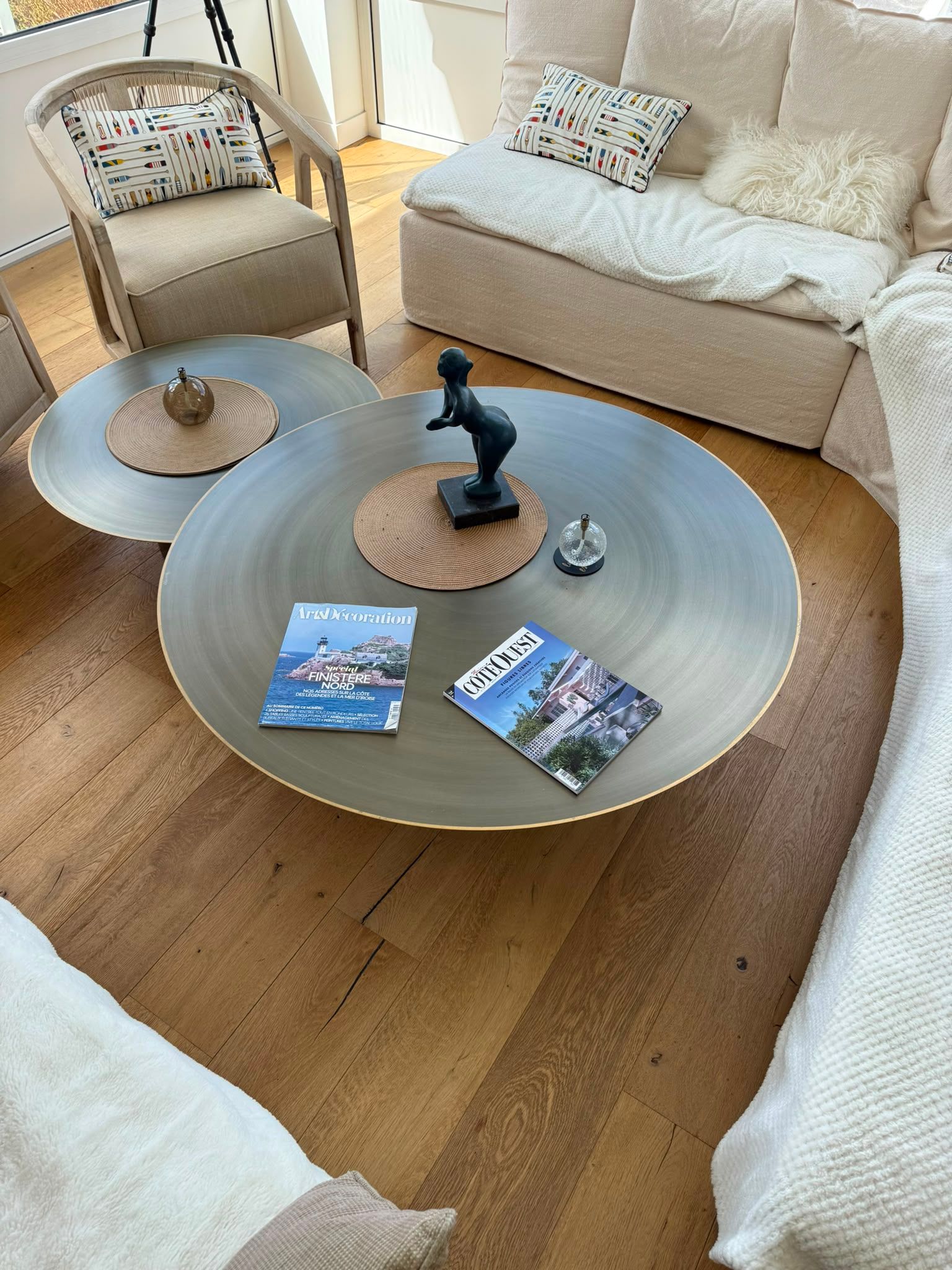 Salon chaleureux avec des canapés beiges, des tables basses rondes et des magazines posés sur un tapis tissé