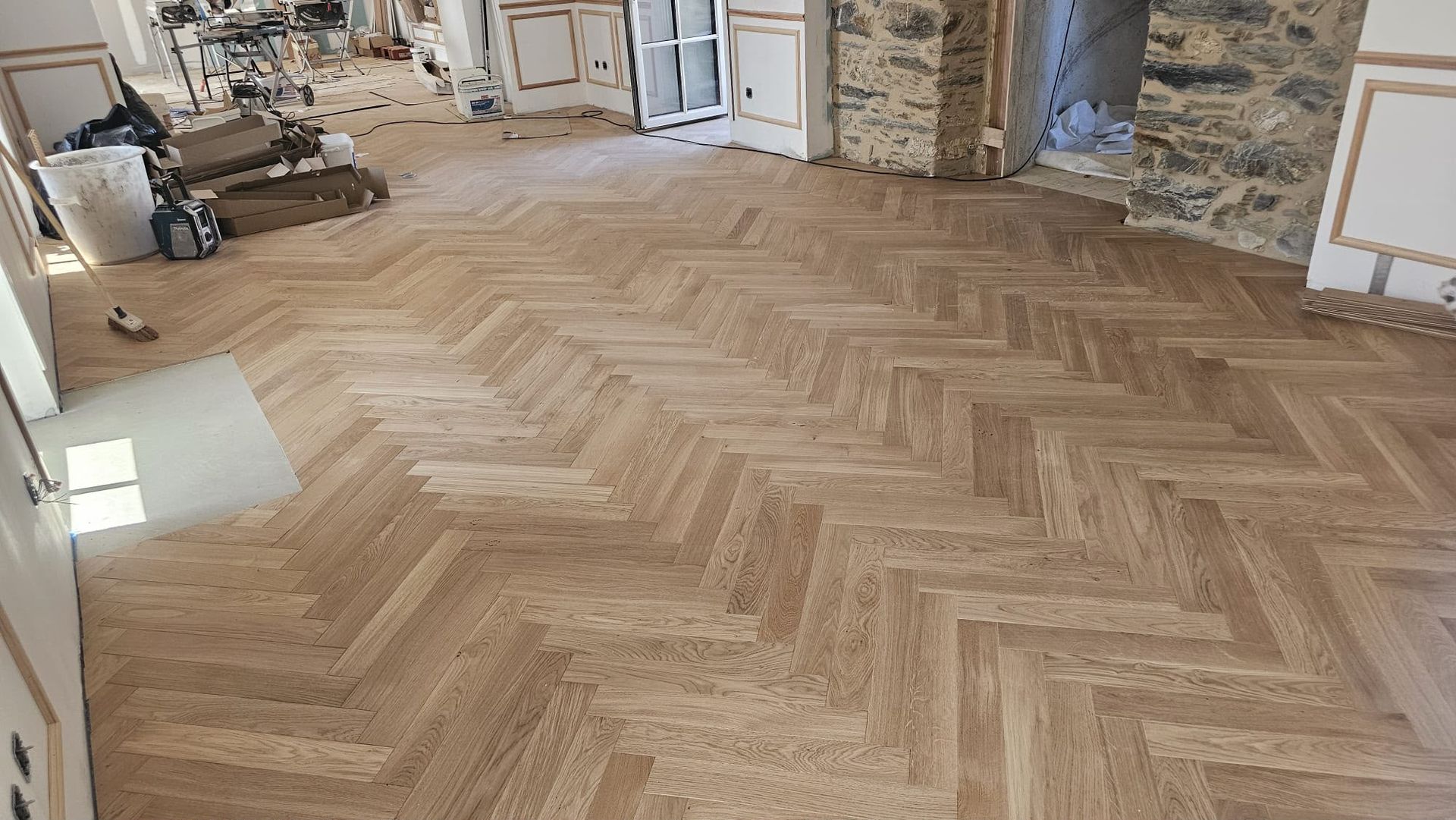 Chambre spacieuse avec un parquet en bois à chevrons tout juste posé et des murs en pierre apparente.