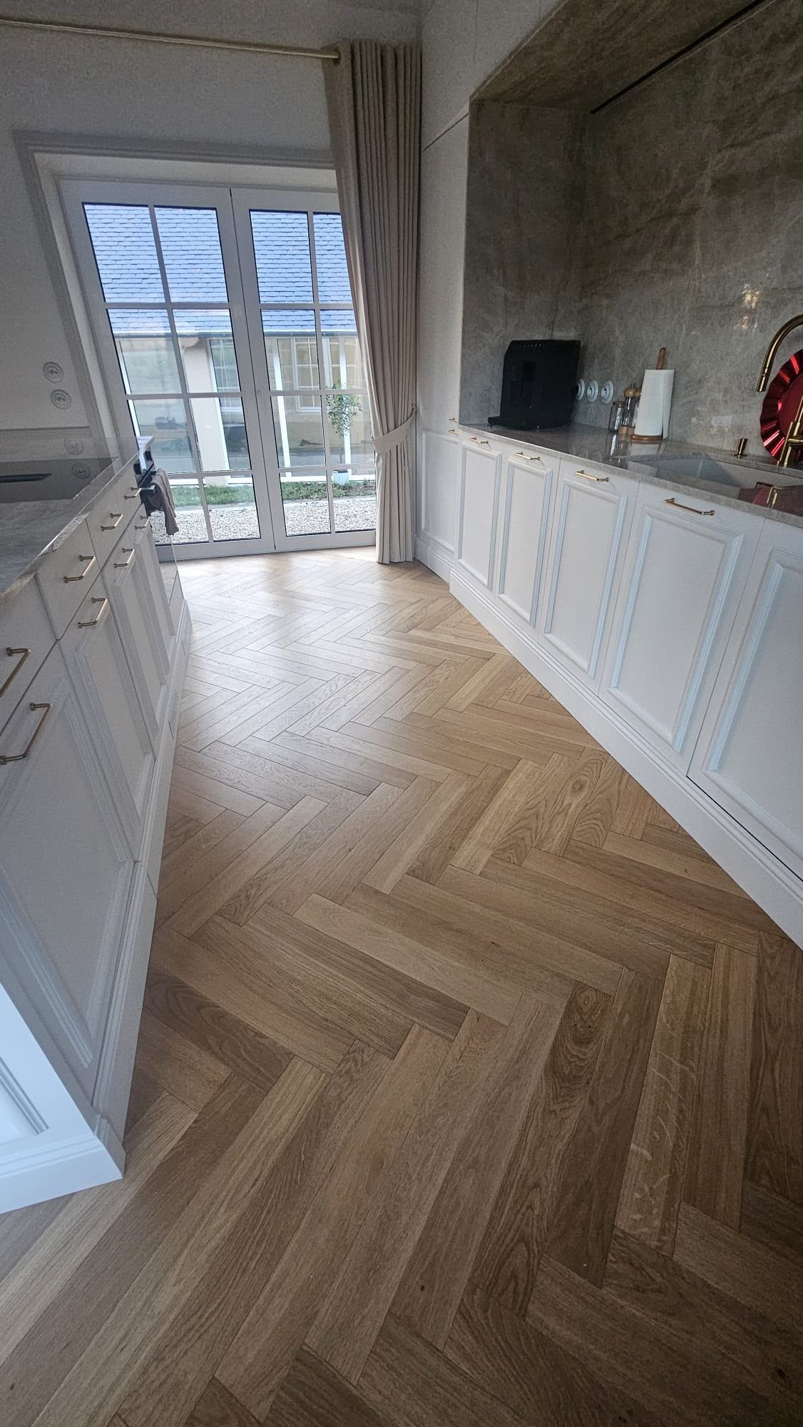 Couloir lumineux avec parquet en chevrons, placards blancs et portes vitrées donnant sur un balcon