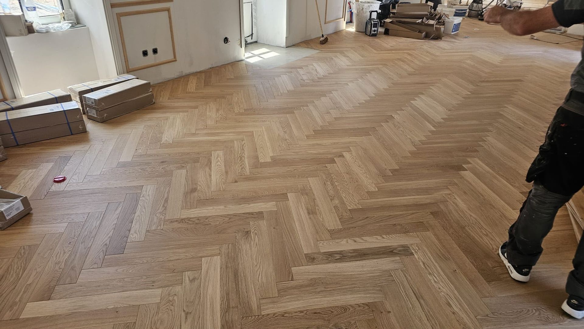 Des ouvriers posent un parquet en bois à chevrons dans une pièce en cours de rénovation
