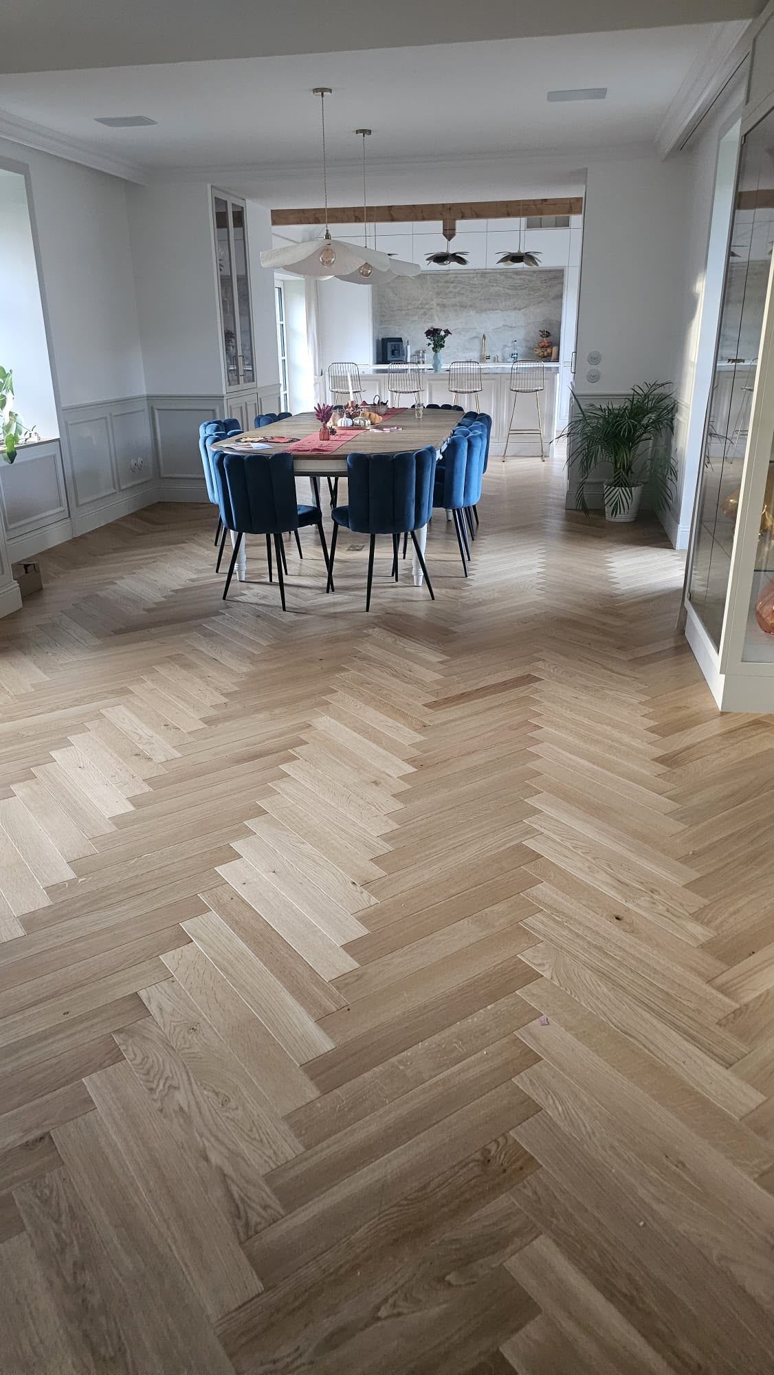 Salle à manger avec parquet en chevrons, chaises bleues et table dans un espace ouvert et lumineux.
