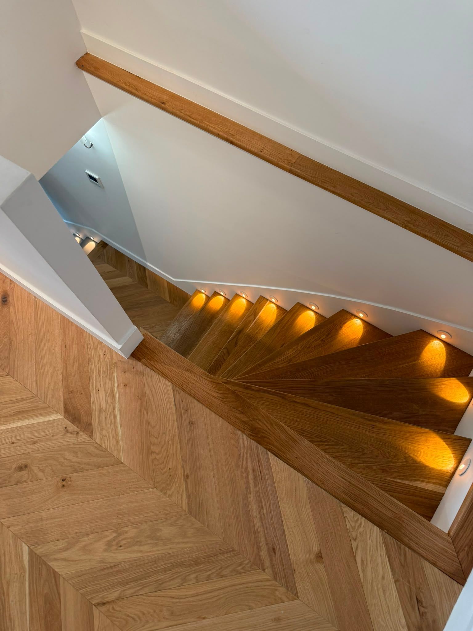 Vue plongeante sur un escalier en bois, éclairé par des lumières chaleureuses