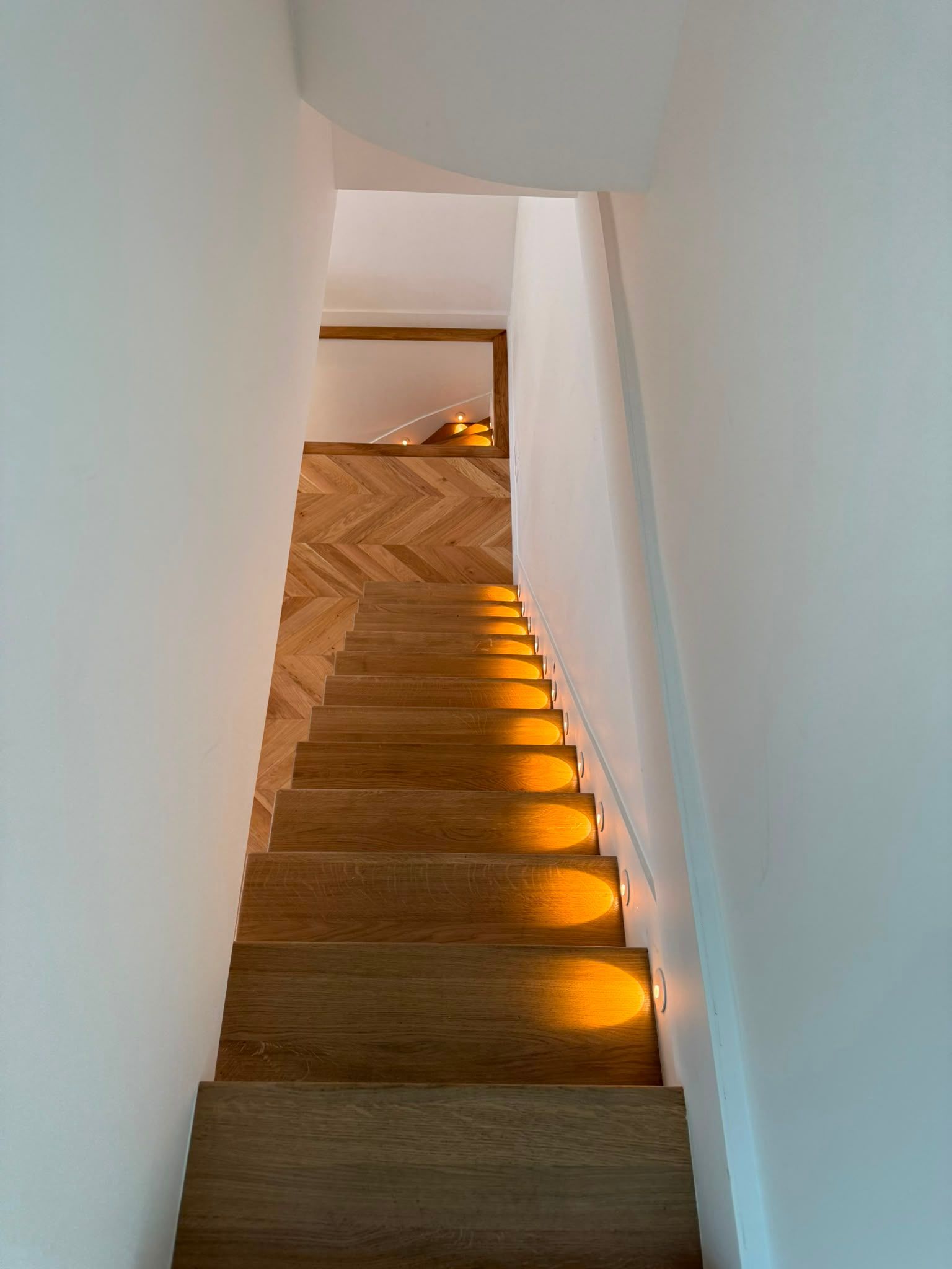 Escalier intérieur étroit, aux murs blancs et éclairé par des lumières chaleureuses