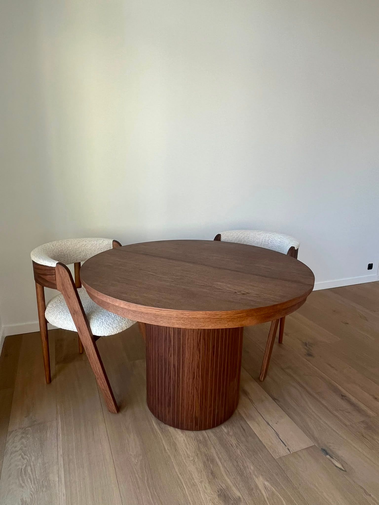 Table à manger ronde en bois avec deux chaises tressées dans une pièce minimaliste