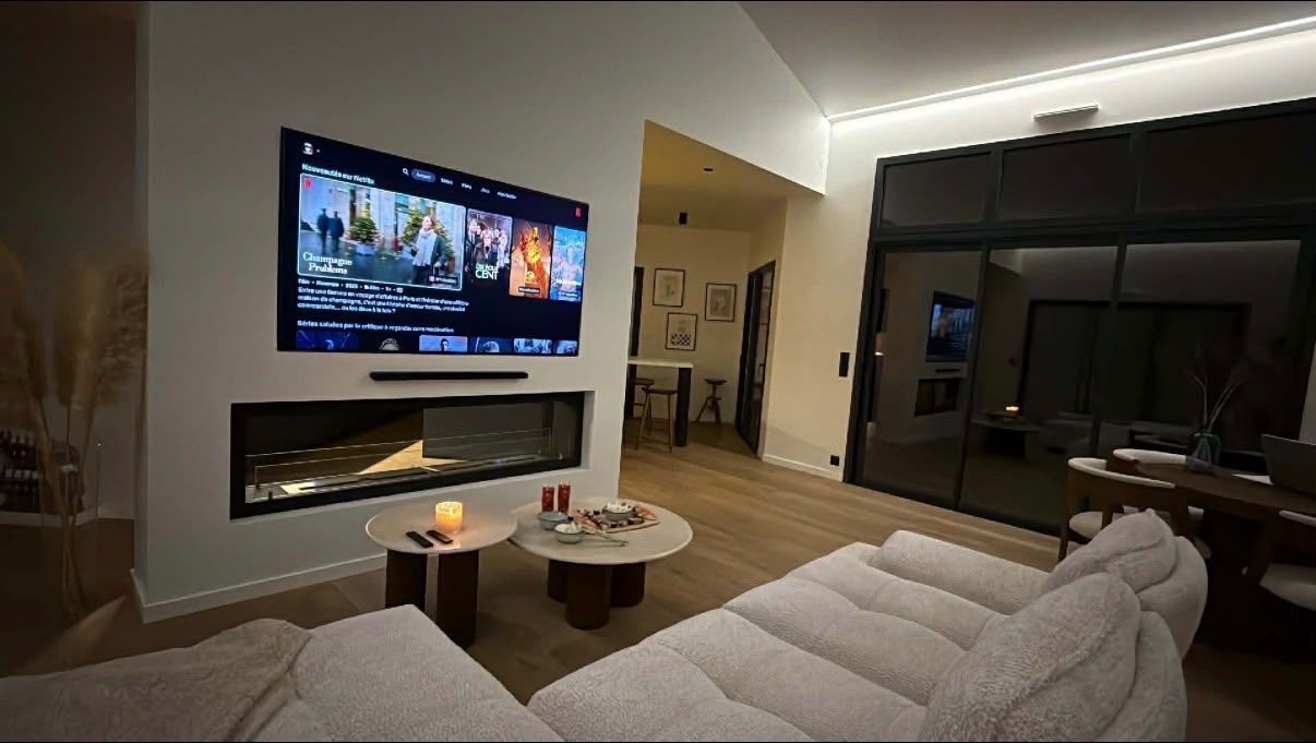 Salon moderne avec une télévision murale, une cheminée, un canapé et des portes vitrées, de nuit