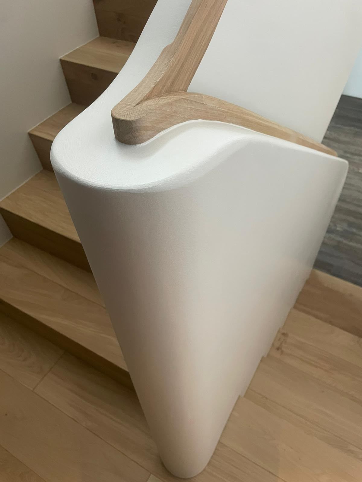 Rampe d’escalier blanche incurvée avec une main courante en bois clair sur un escalier en bois