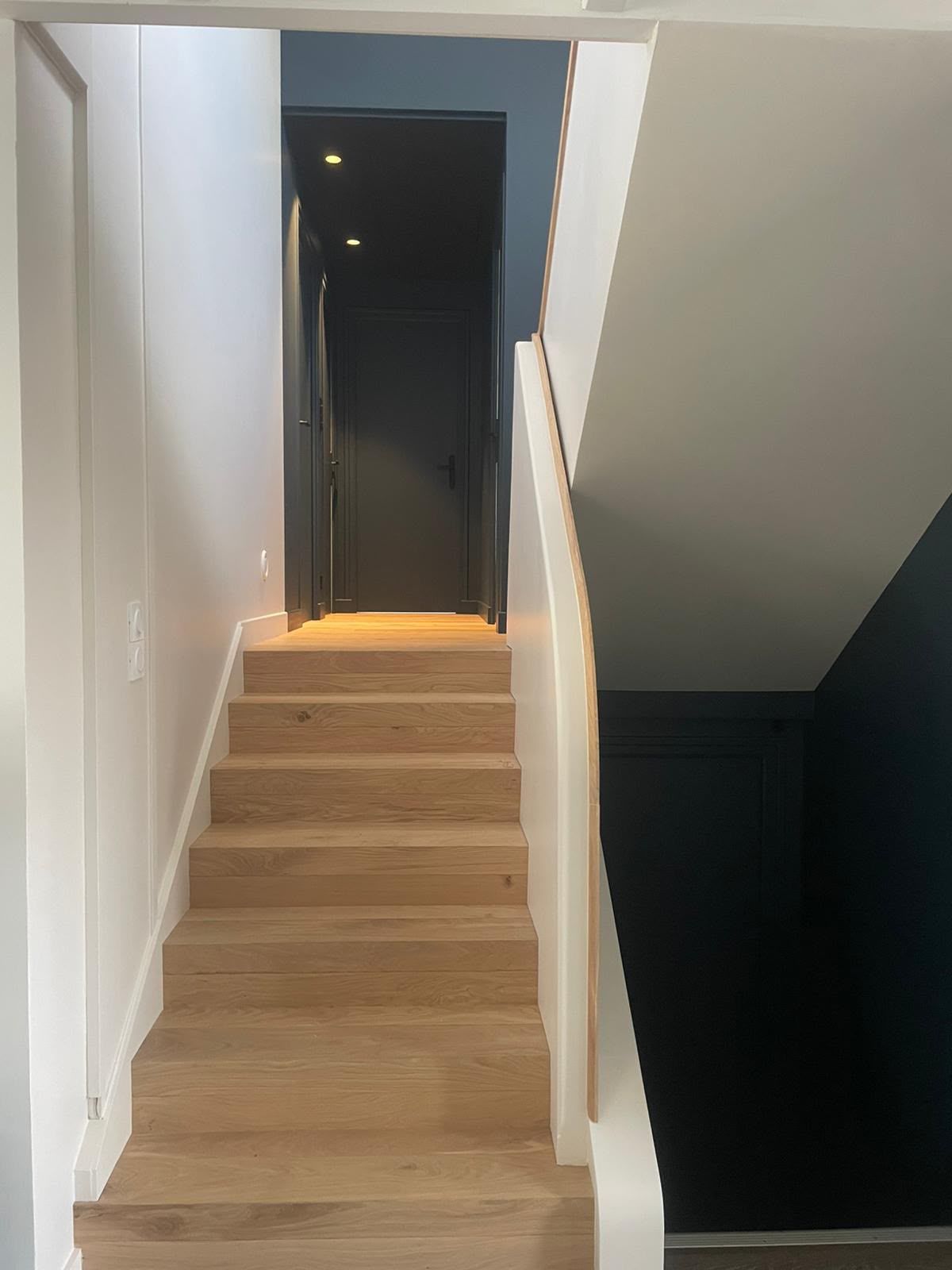 Escalier étroit aux marches en bois menant à une porte sombre dans un intérieur moderne.