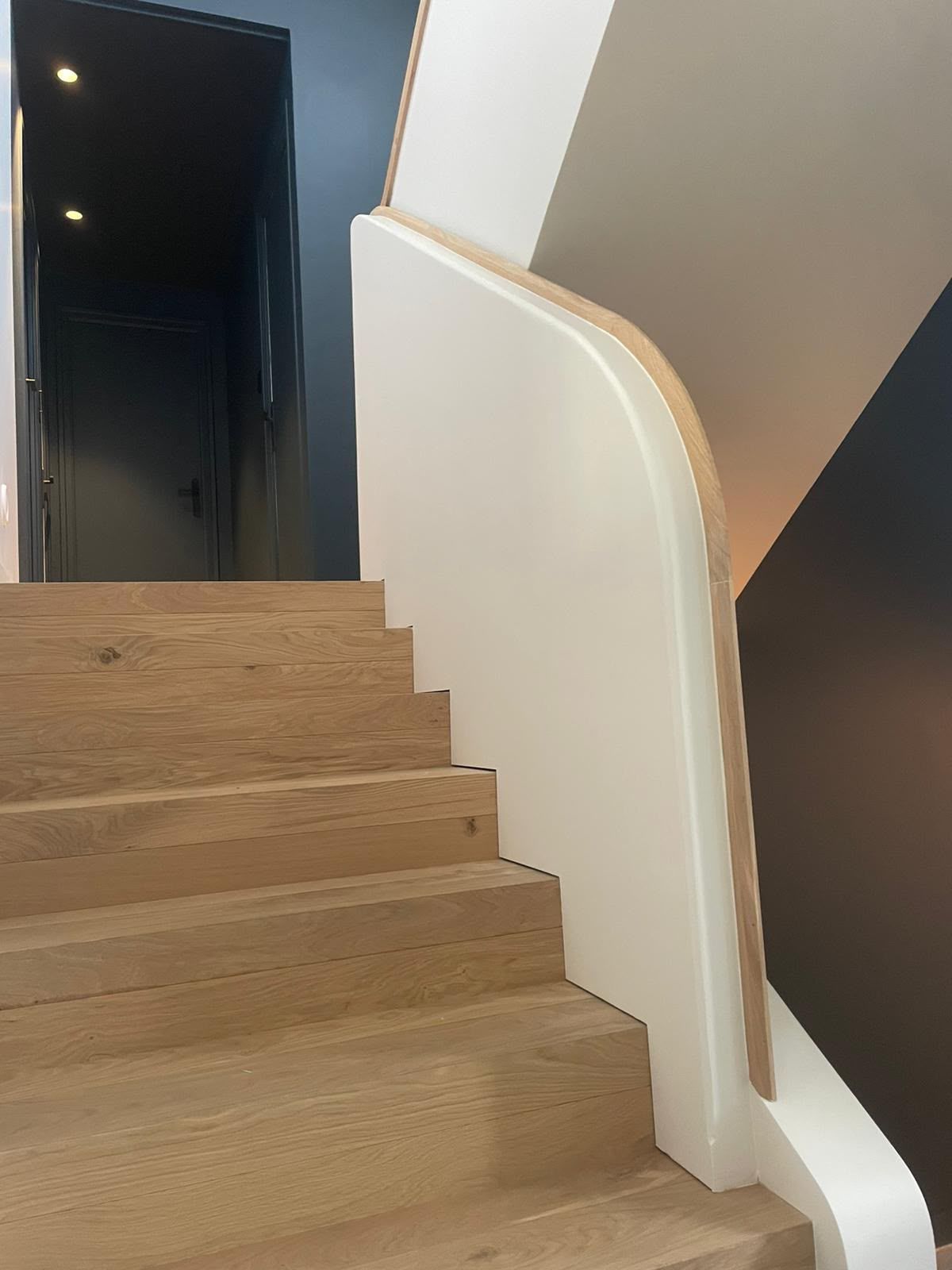 Escalier en bois avec une rampe blanche, à côté d’une porte sombre dans un intérieur moderne