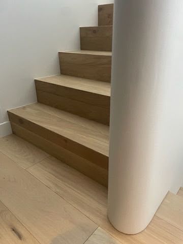 Escalier en bois, murs blancs et colonne blanche arrondie dans un intérieur minimaliste.