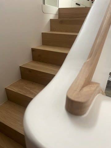 Escalier en bois avec des murs blancs et une main courante en bois clair, vu du bas.