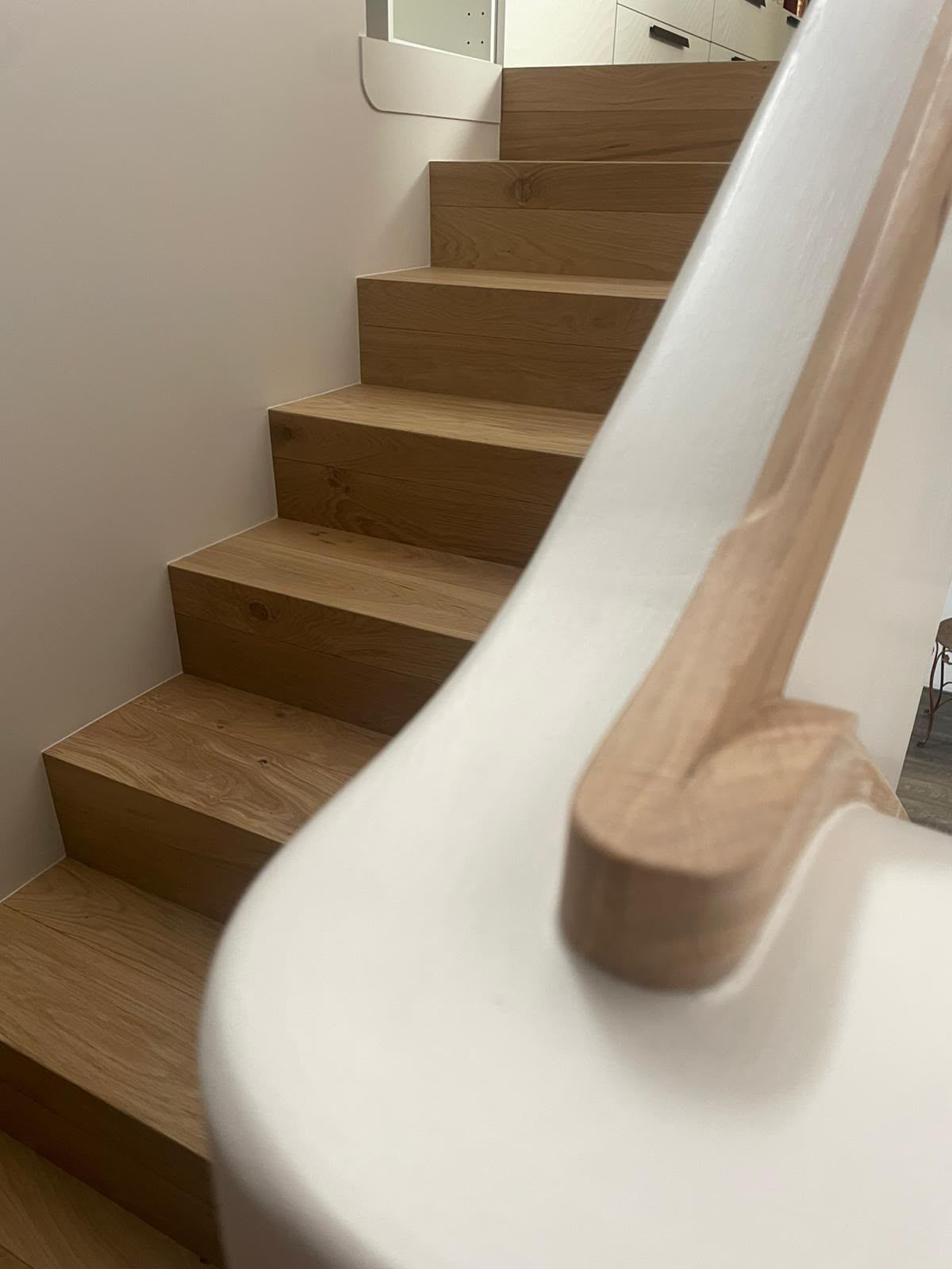 Escalier en bois, murs clairs et rampe blanche incurvée dans un intérieur moderne.