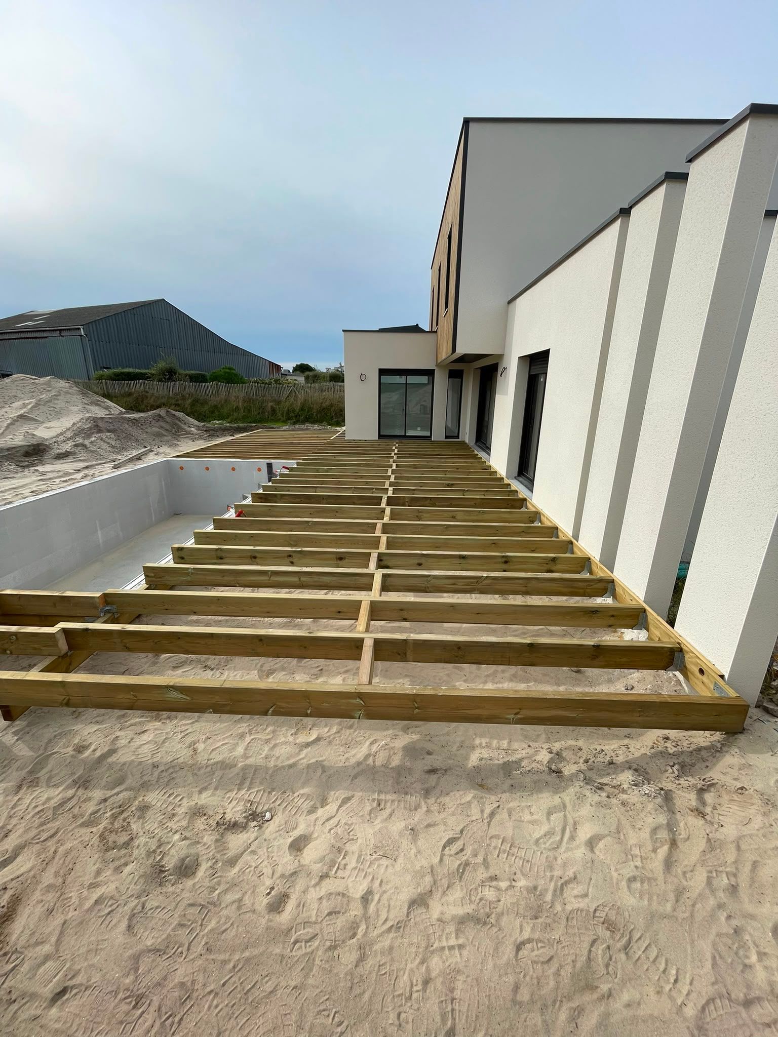 Ossature d’une terrasse en bois à côté d’une maison blanche en construction