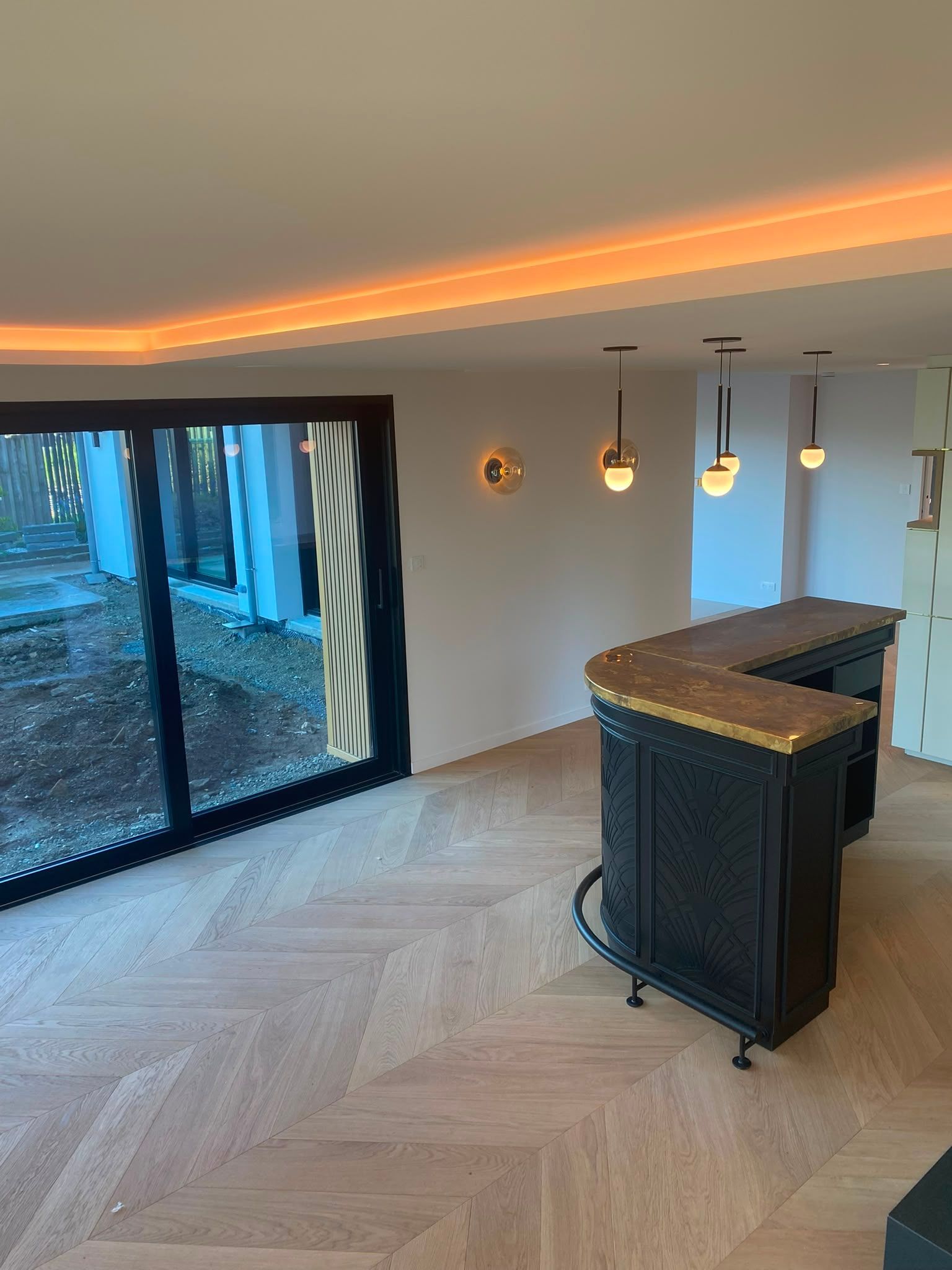 Cuisine moderne avec parquet en chevrons, îlot foncé, suspensions et grandes baies vitrées coulissantes