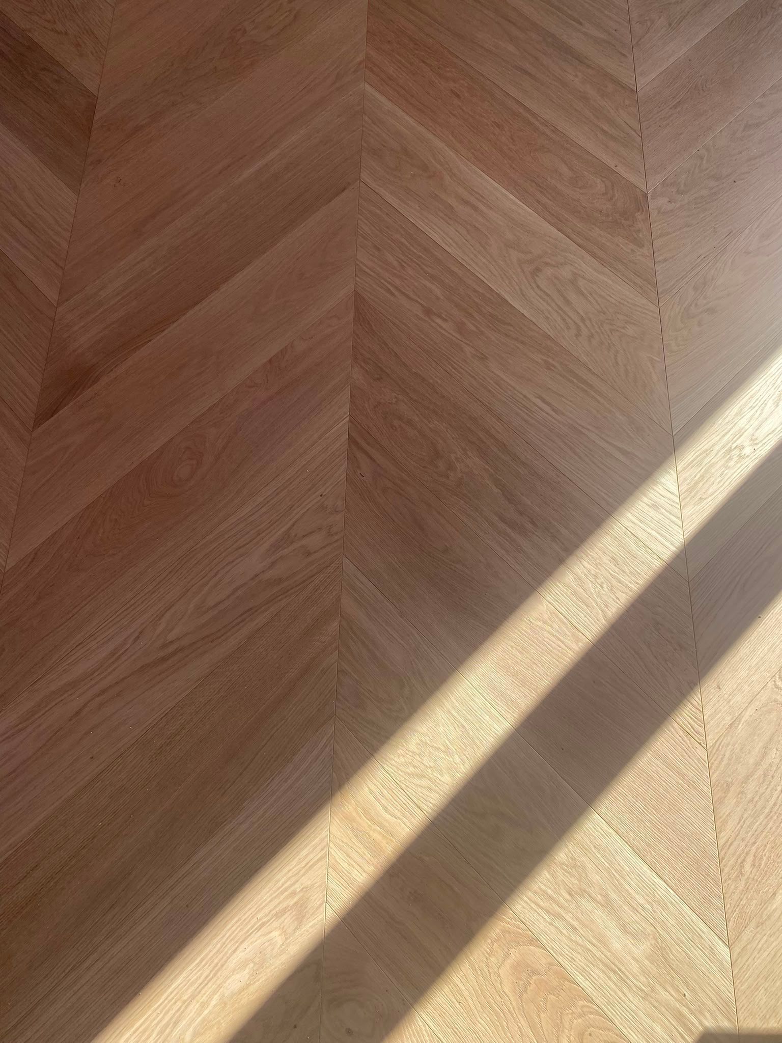 Parquet en bois à chevrons, baigné de soleil et traversé d’ombres diagonales