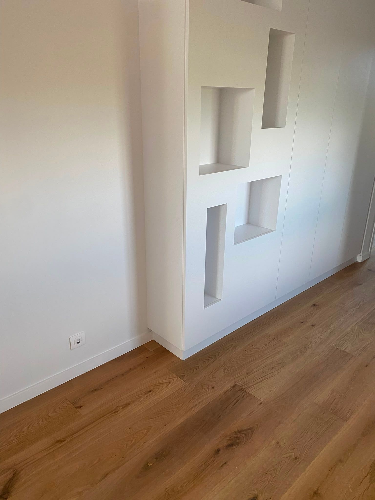 Pièce vide avec un parquet et un mur blanc doté de niches carrées encastrées.