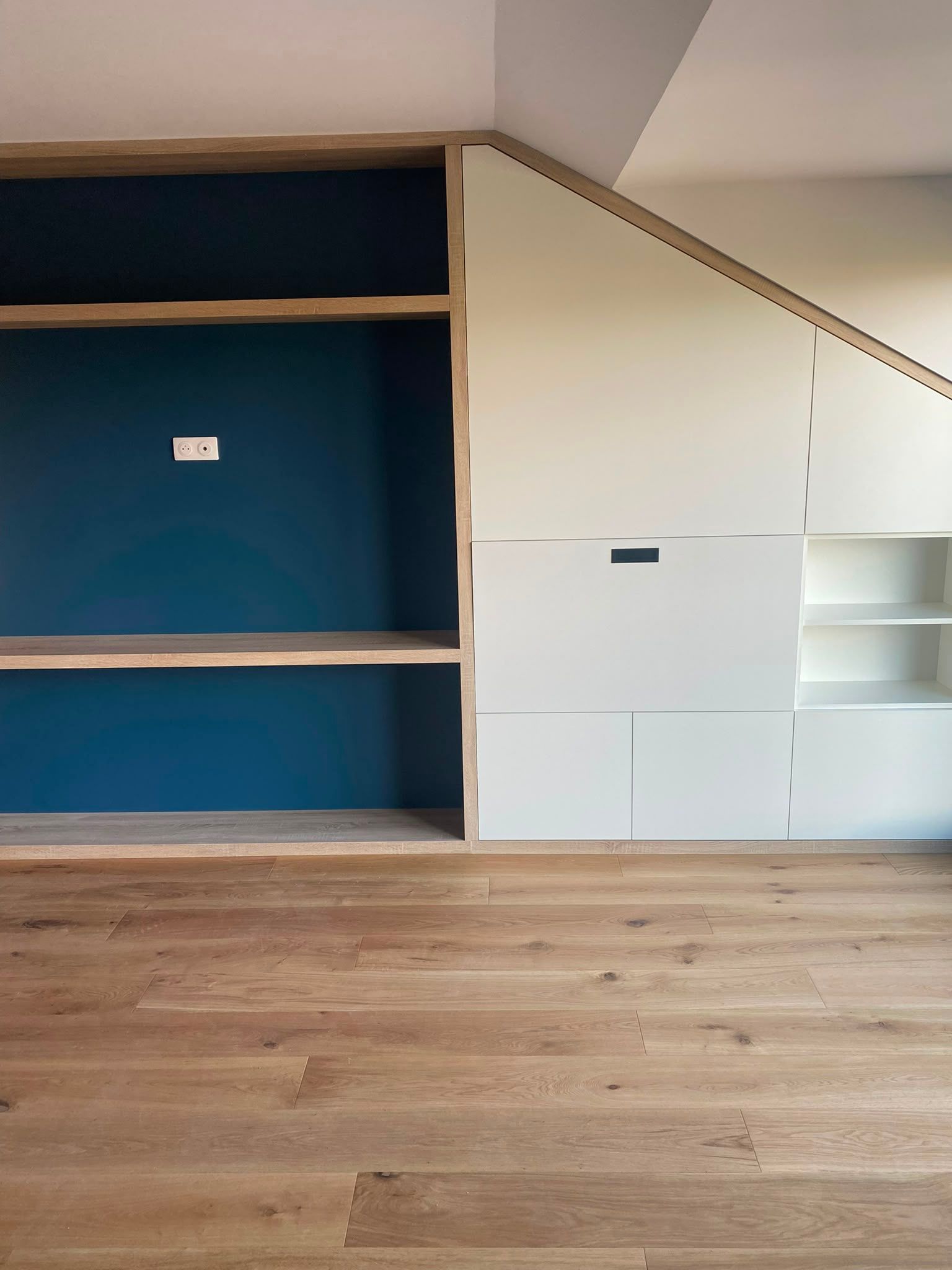 Mur de rangement intégré avec des étagères bleues, des placards blancs et un parquet en bois dans une pièce.