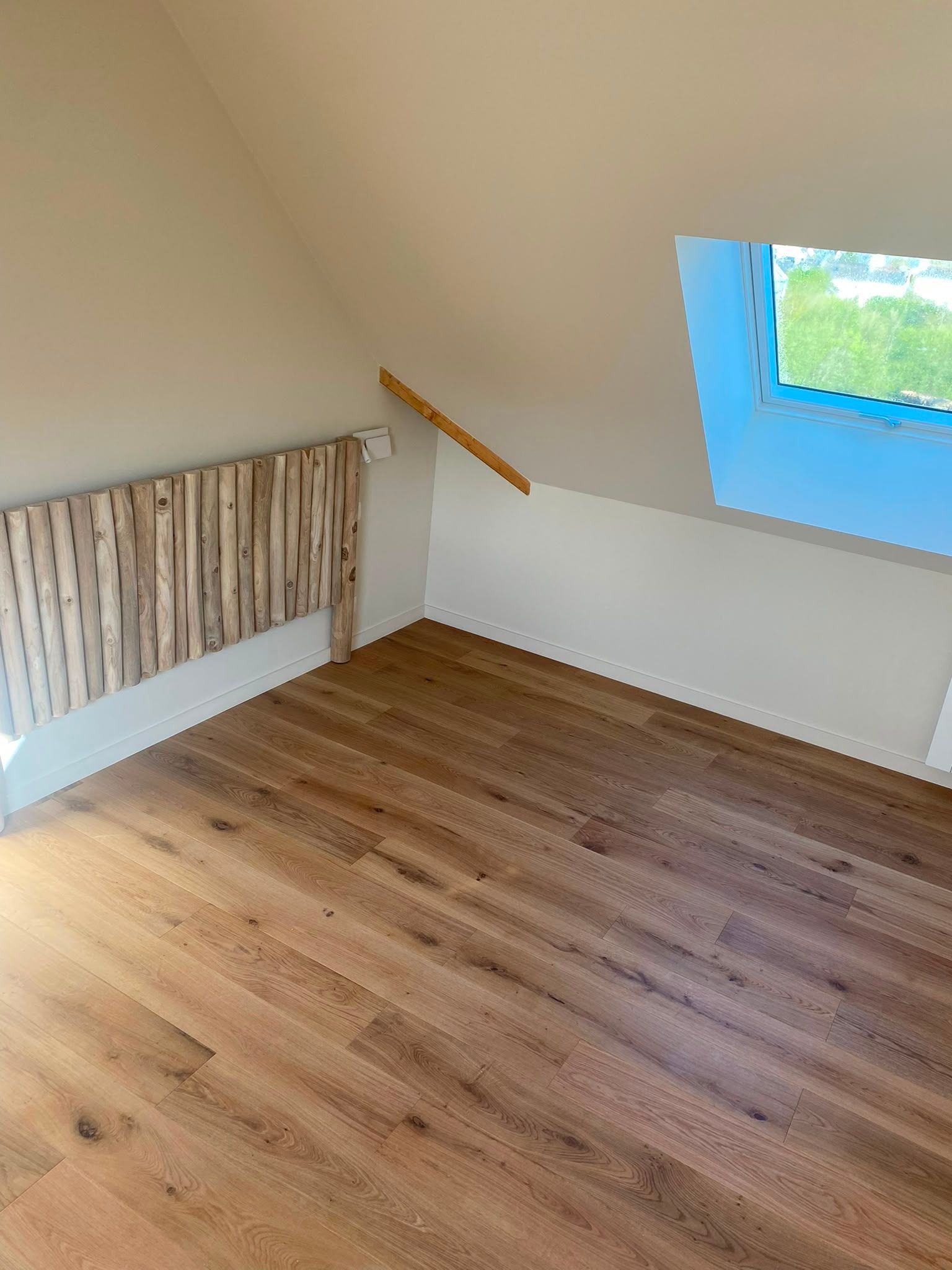 Combles vides avec plafond en pente, parquet et petite fenêtre.