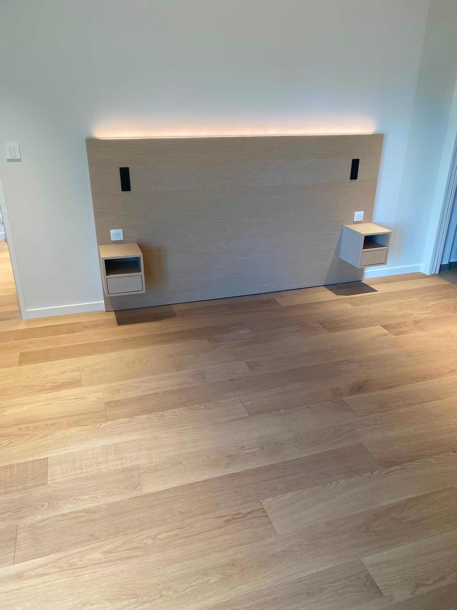 Chambre minimaliste avec parquet, tête de lit fixée au mur, tables de chevet et éclairage indirect doux