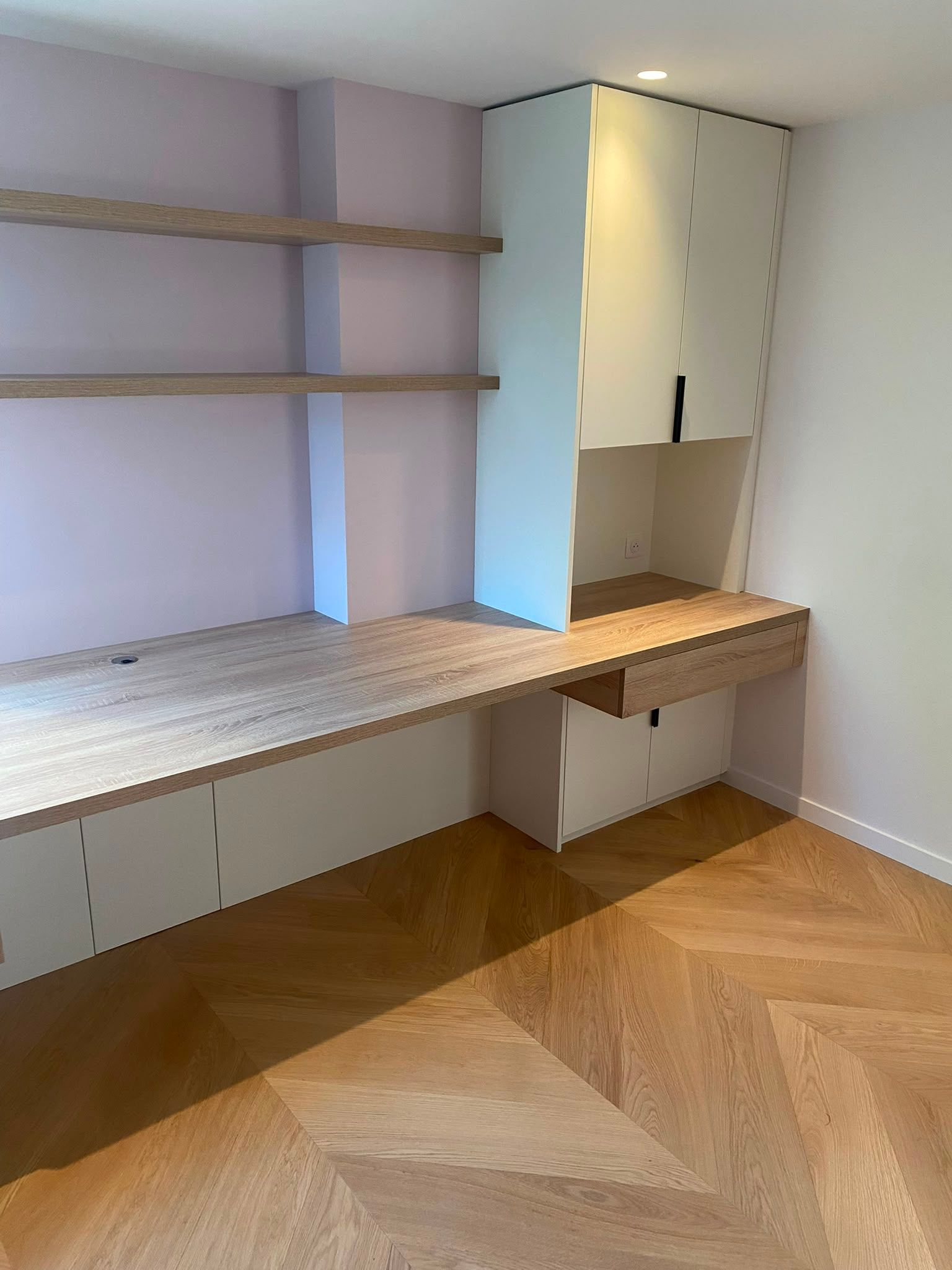 Coin bureau intégré avec des étagères en bois, des placards et un parquet clair à chevrons dans une pièce blanche