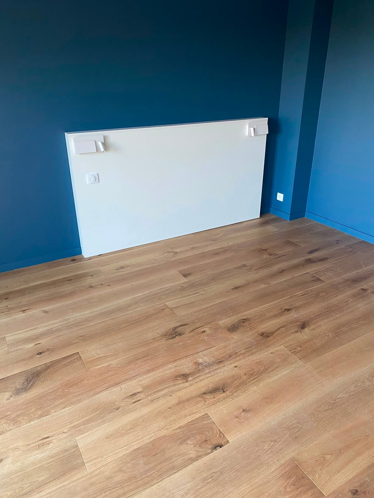 Pièce vide aux murs bleus, avec un parquet en bois et un cache-radiateur blanc contre le mur du fond