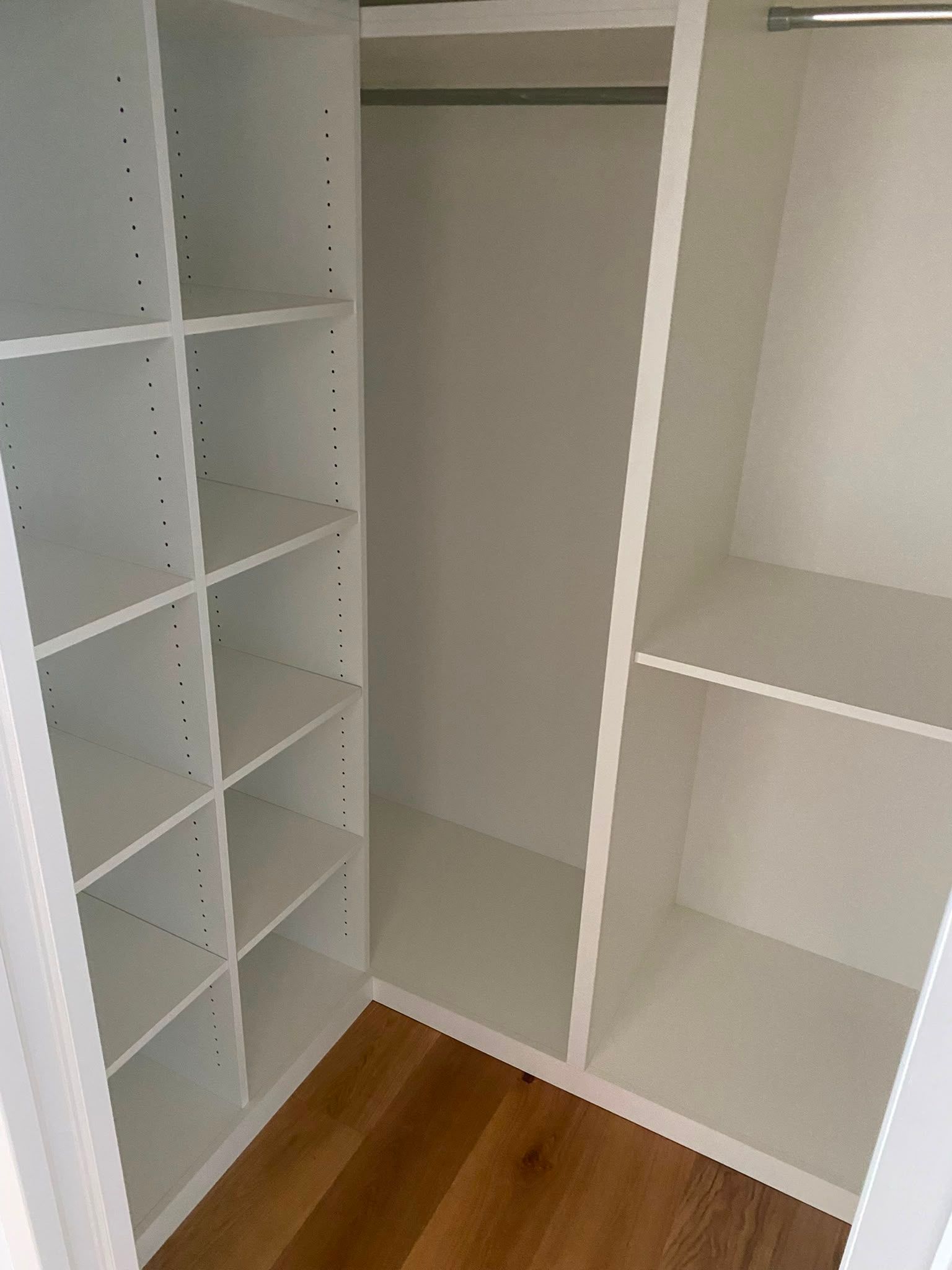 Dressing-room blanc vide avec des étagères, une tringle et un parquet en bois.