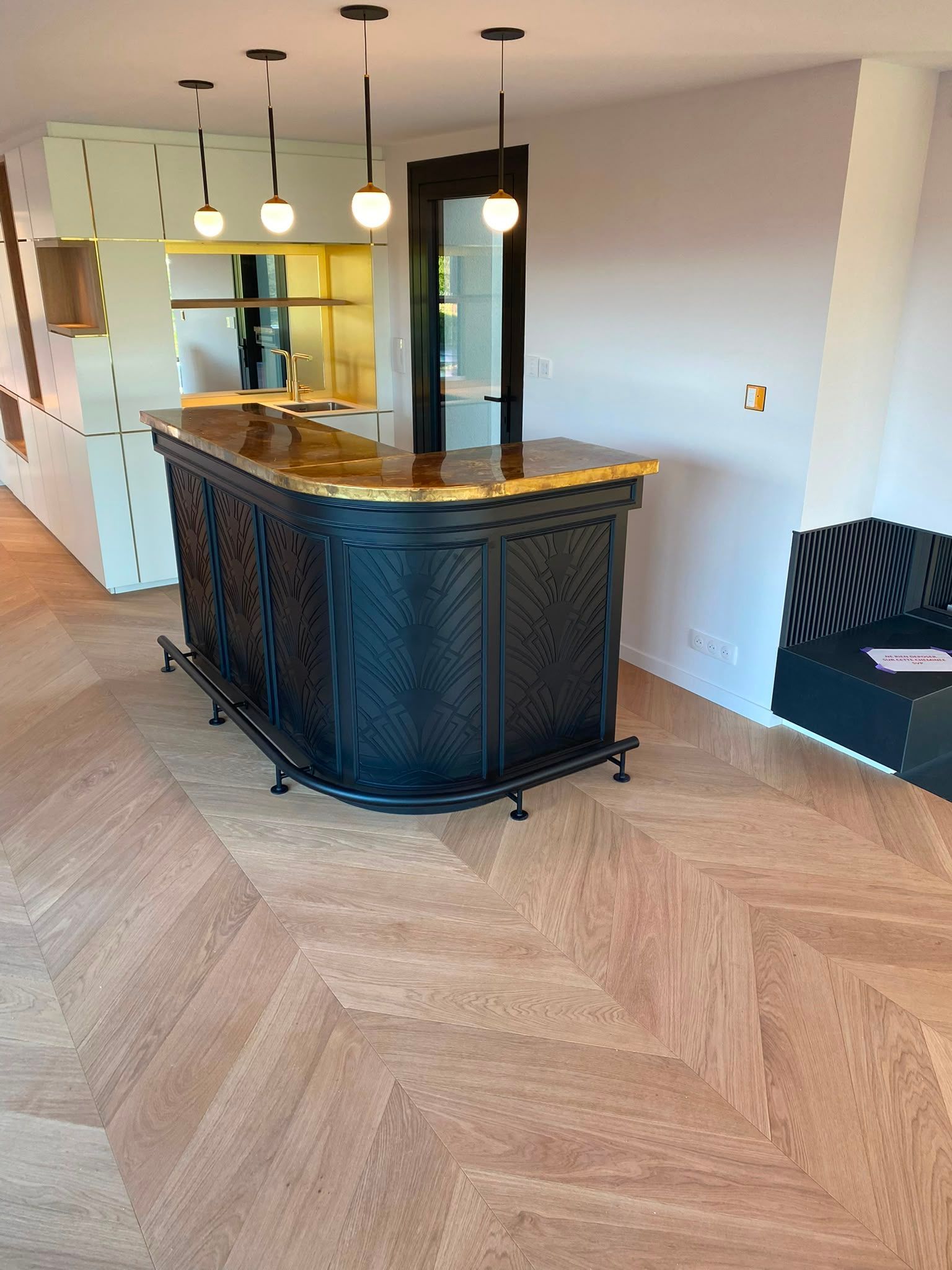 Cuisine moderne avec un îlot sombre aux formes arrondies, des suspensions, un parquet en chevrons et un espace salon attenant