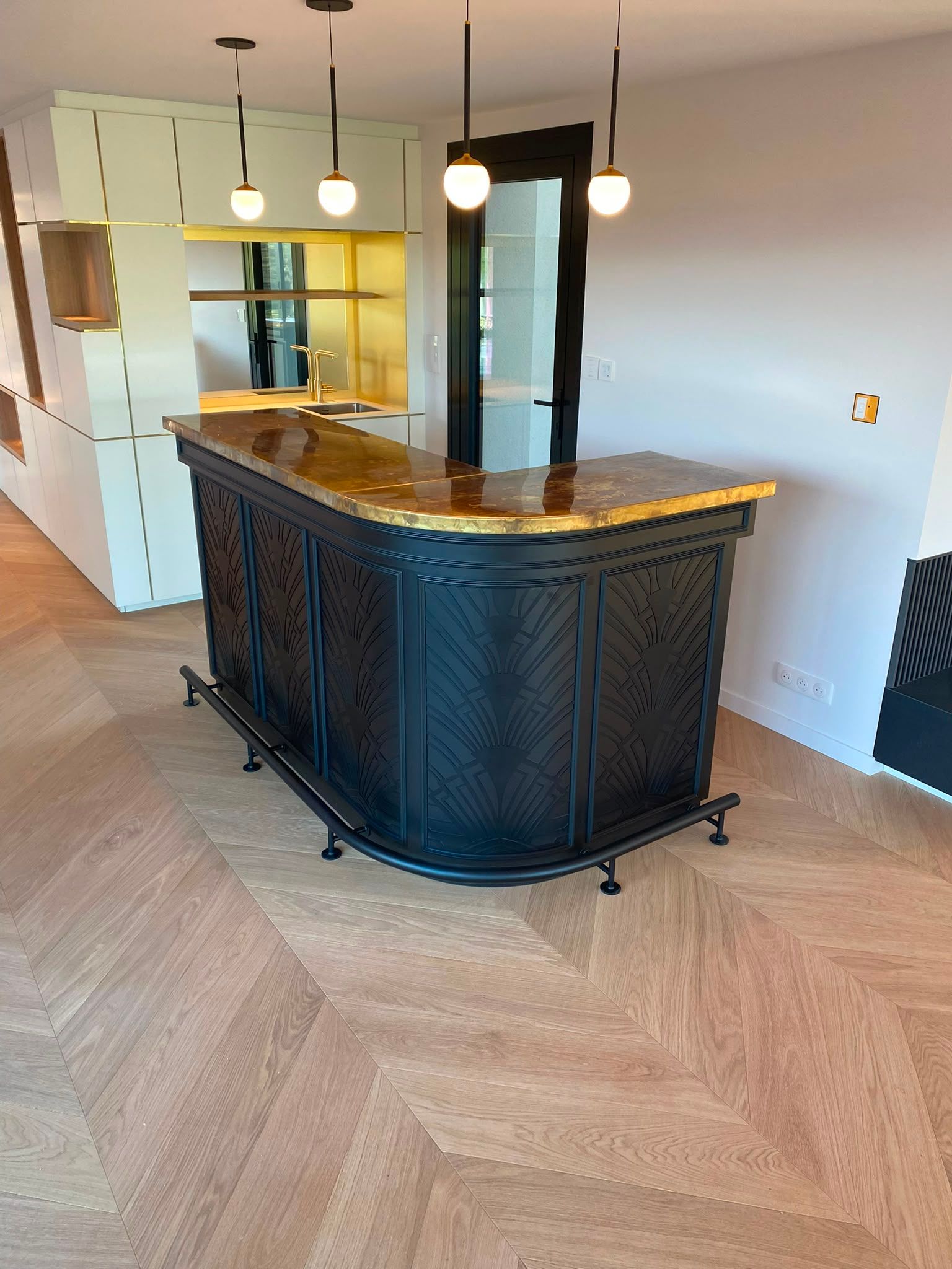 Pièce vide avec un comptoir de bar en bois foncé, des suspensions lumineuses et un parquet à chevrons