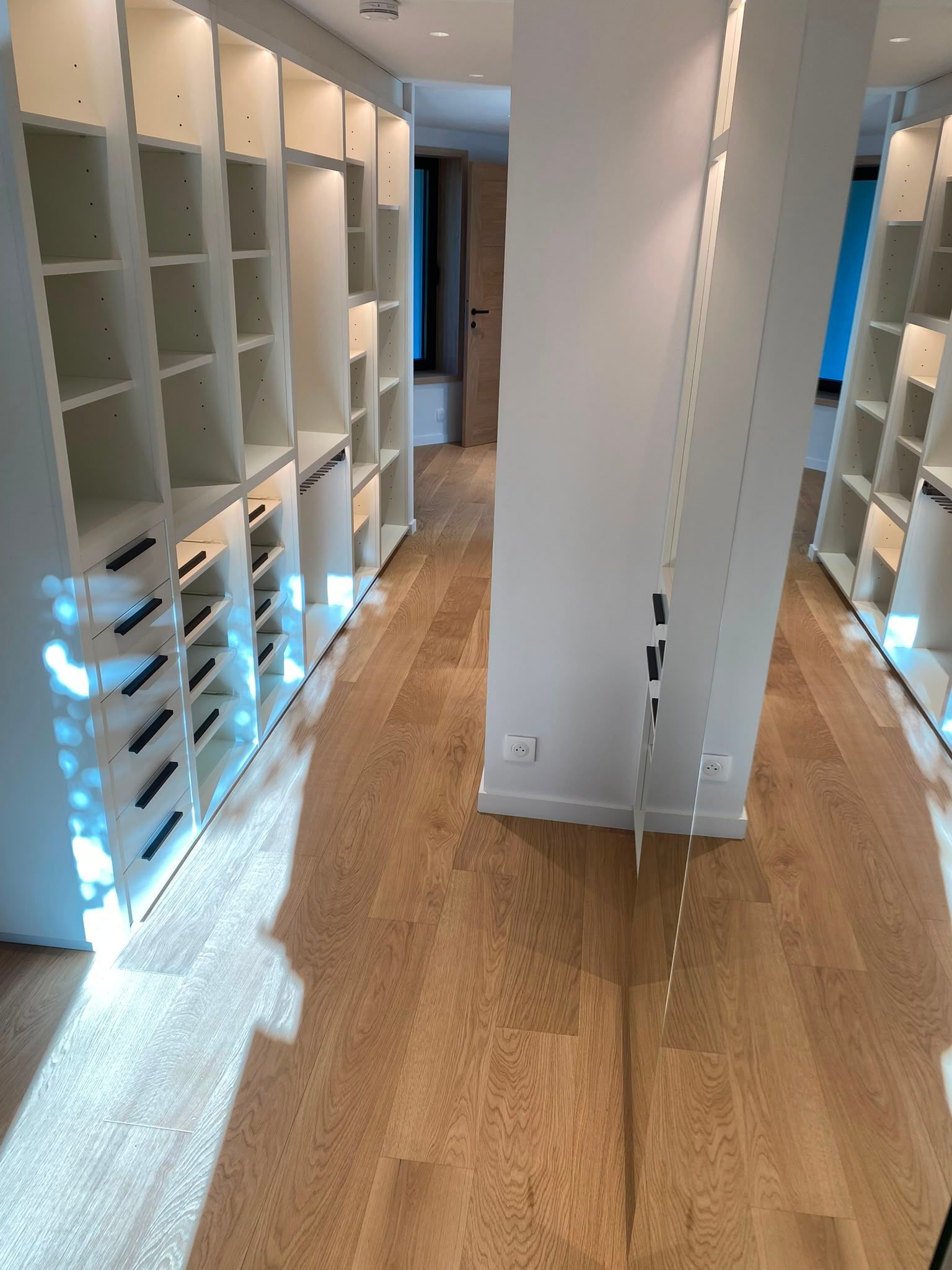 Couloir vide avec des étagères blanches intégrées et un parquet dans un intérieur lumineux.