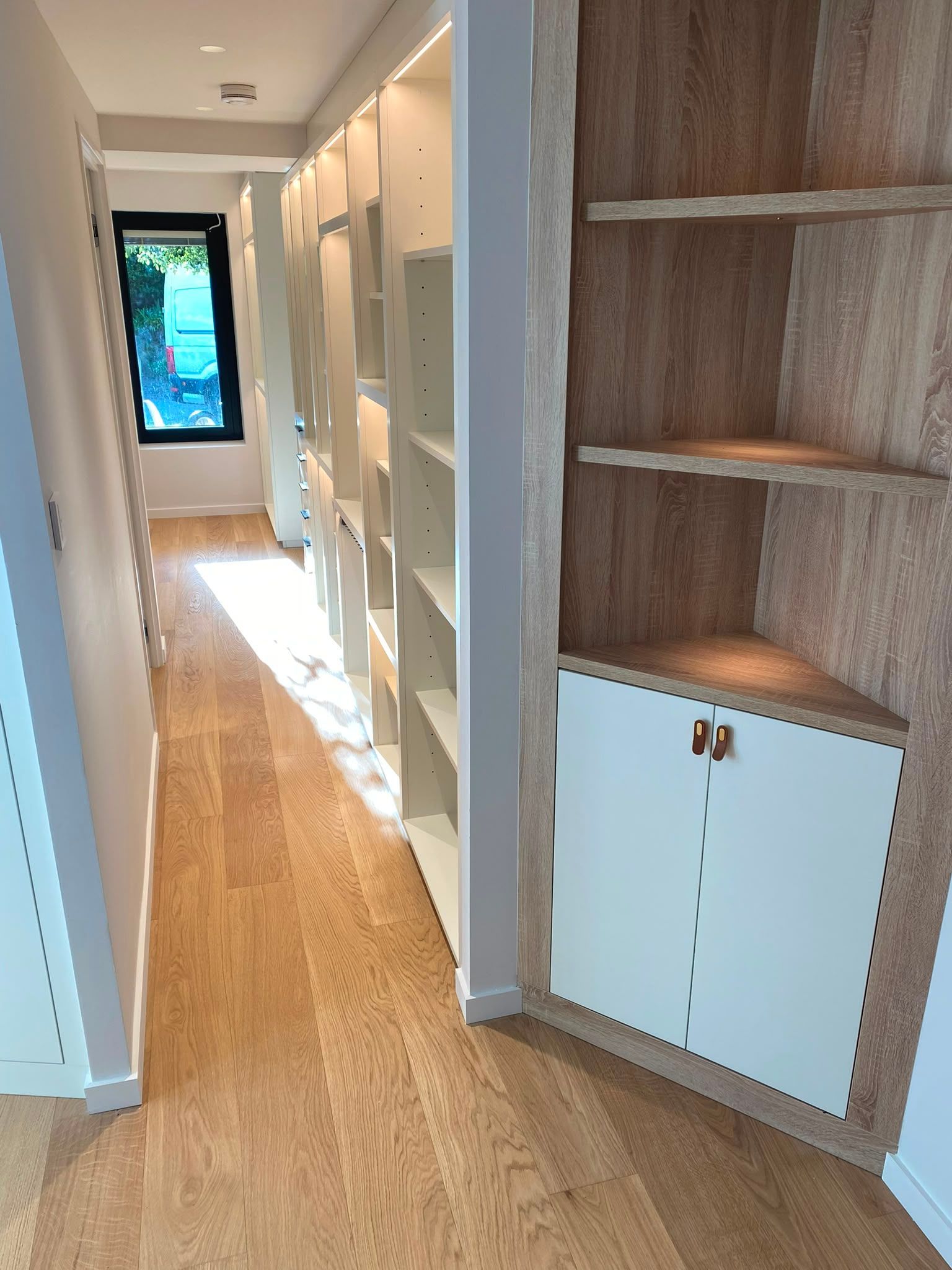 Couloir lumineux avec un parquet et des étagères/placards intégrés, qui mène à une porte vitrée.