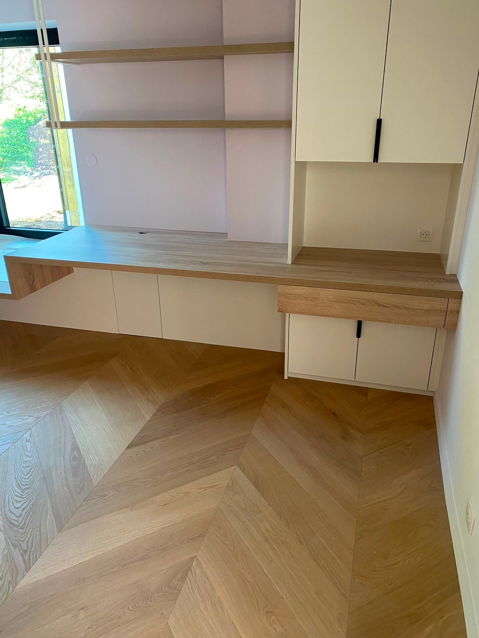 Étagères blanches intégrées et coin bureau dans une pièce au parquet clair en chevrons