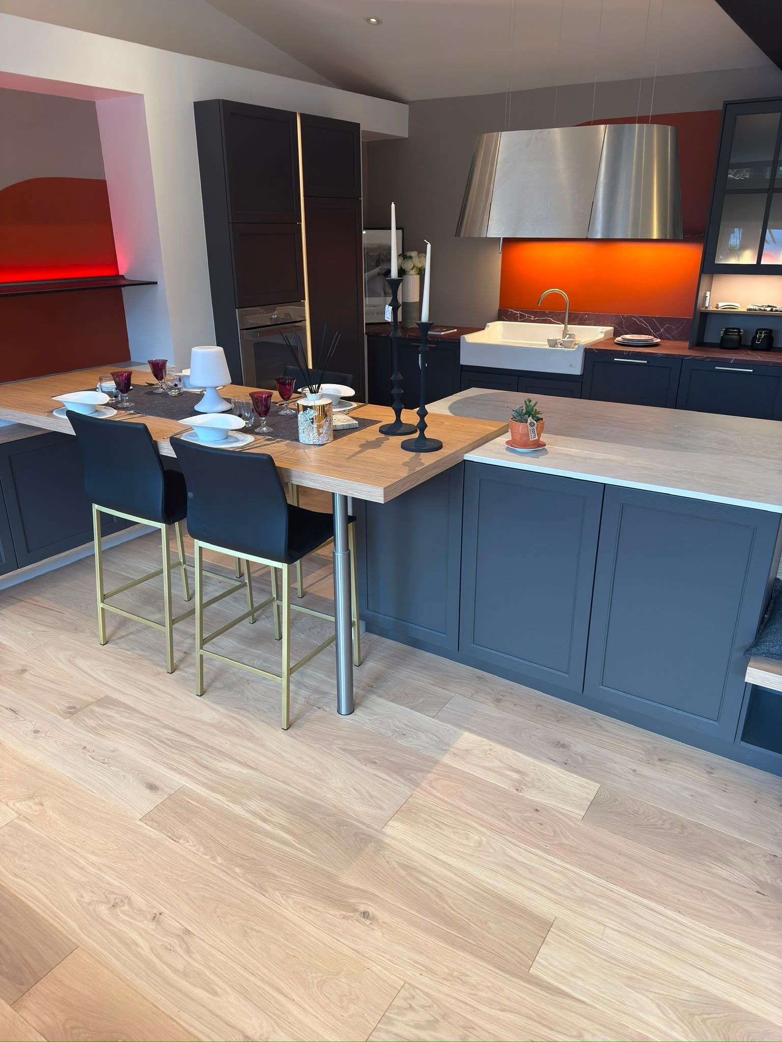 Cuisine moderne avec des meubles bleus, un îlot en bois, des tabourets de bar noirs et une crédence orange