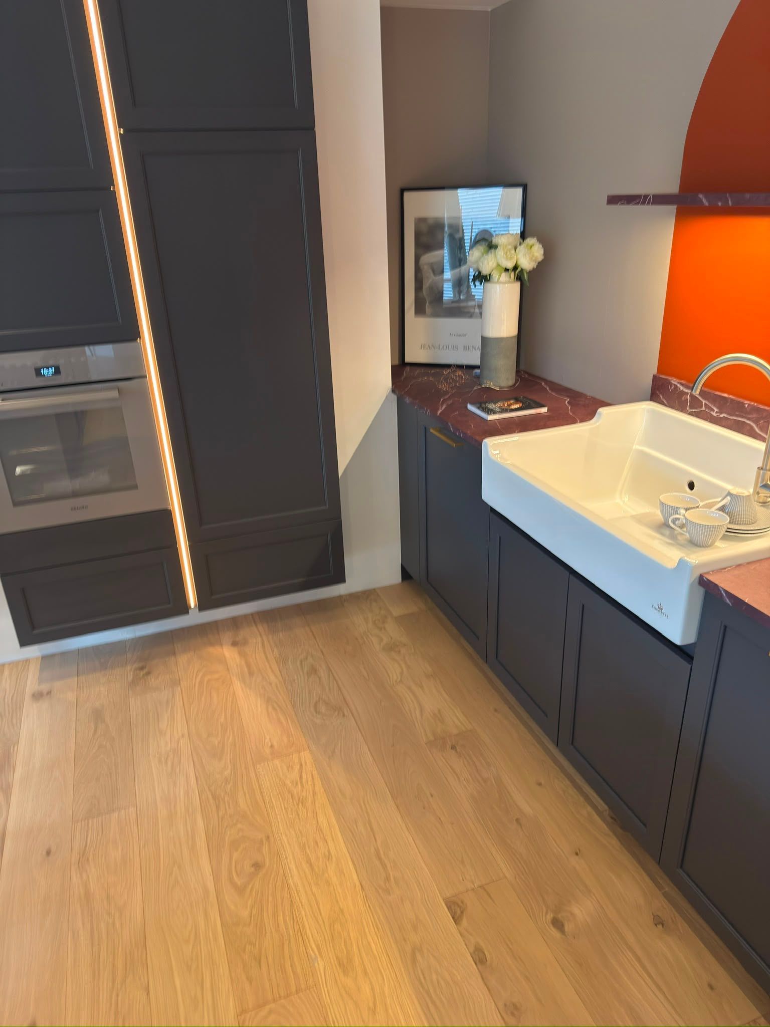 Salle de bains moderne avec des meubles foncés, un lavabo blanc, un mur d’accent orange et un parquet en bois.