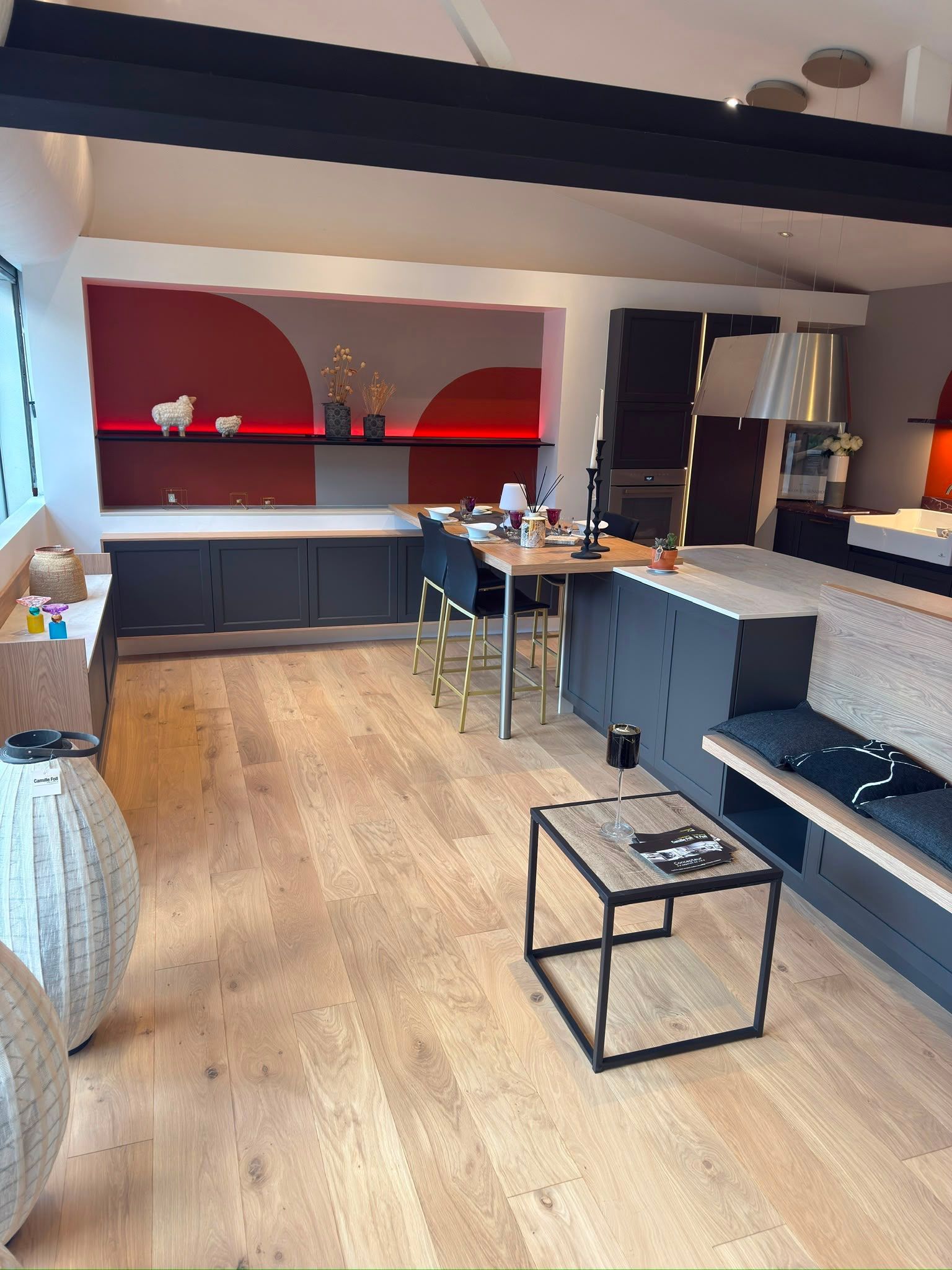 Salon moderne à aire ouverte avec parquet, canapé gris, table basse noire et étagères aux accents rouges.