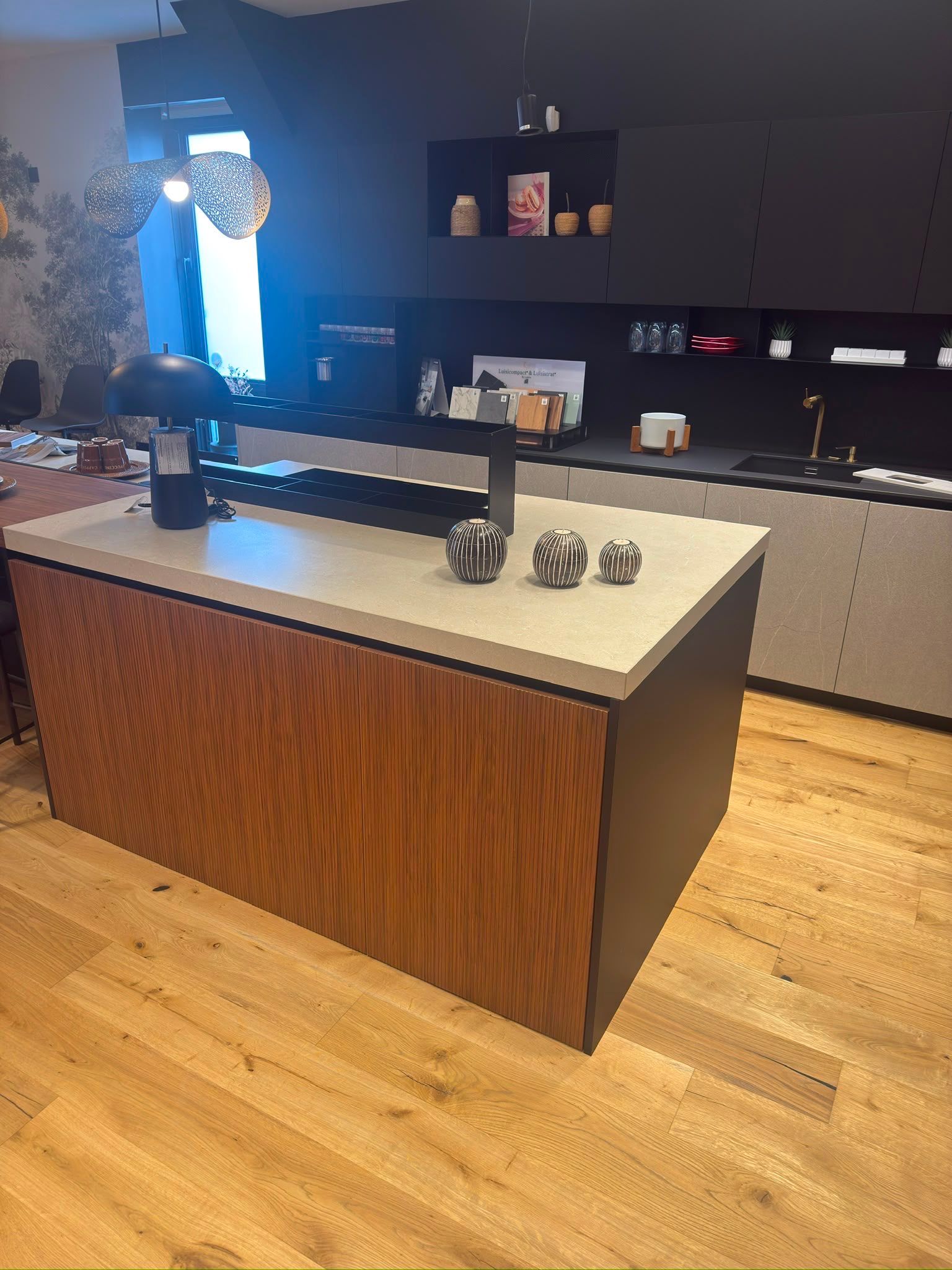 Cuisine moderne avec îlot en bois, plan de travail blanc, placards foncés et parquet.