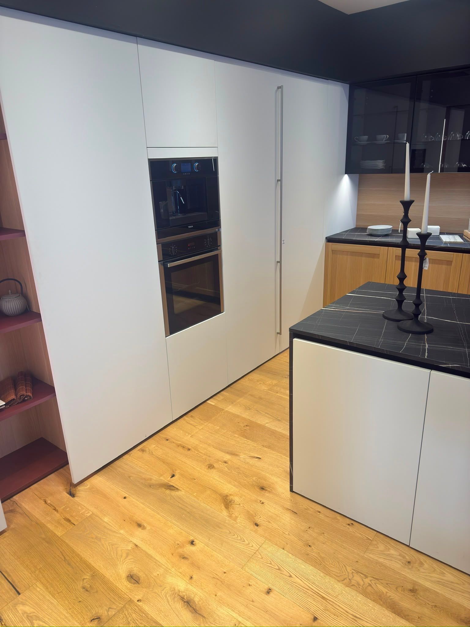 Cuisine moderne avec des placards blancs, un four encastré, un sol en bois et un îlot avec un plan de travail noir