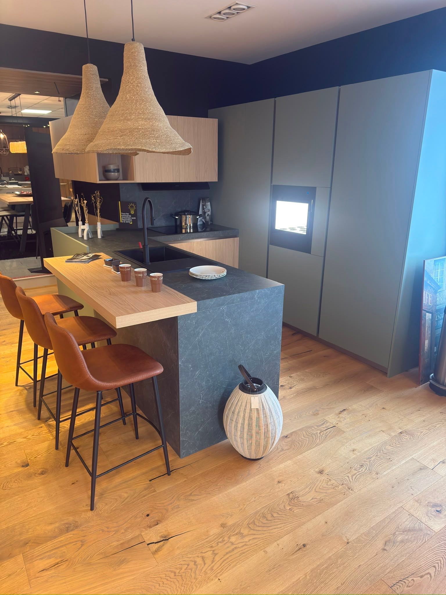 Cuisine moderne avec îlot central, suspensions tressées, tabourets de bar et placards gris.