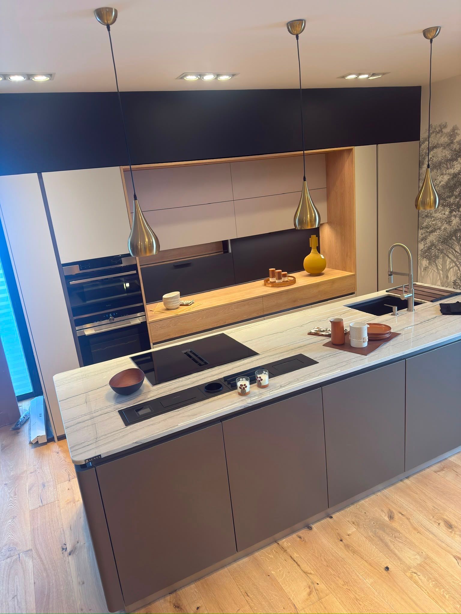 Cuisine moderne avec îlot, meubles foncés, parquet, évier et plaque de cuisson en acier inoxydable