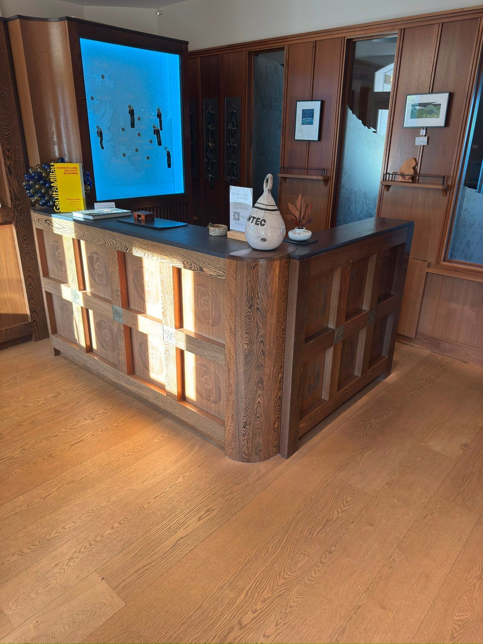 Comptoir d’accueil en bois dans un hall, avec des écrans muraux et un éclairage au sol