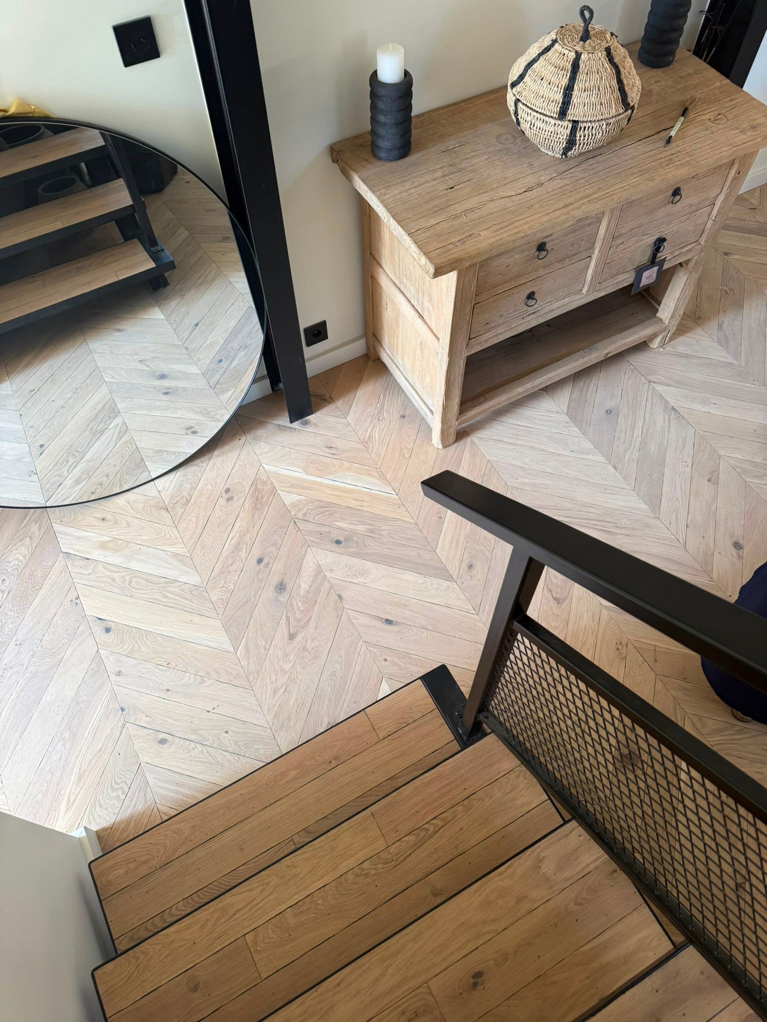 Entrée moderne avec un miroir rond, une console en bois et un banc tressé sur un sol à chevrons.