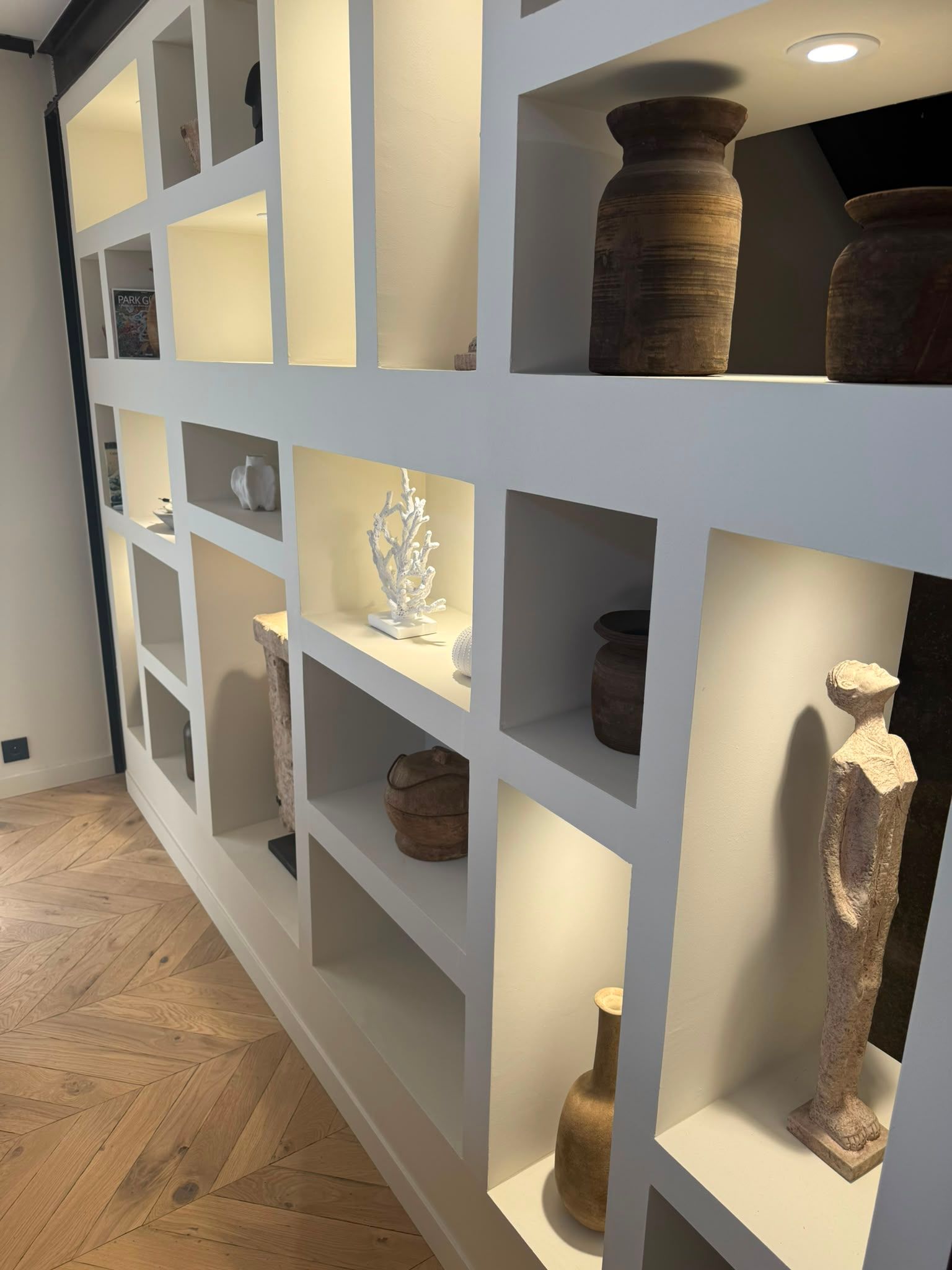 Étagères intégrées blanches exposant des poteries et des sculptures dans un couloir à l’éclairage tamisé