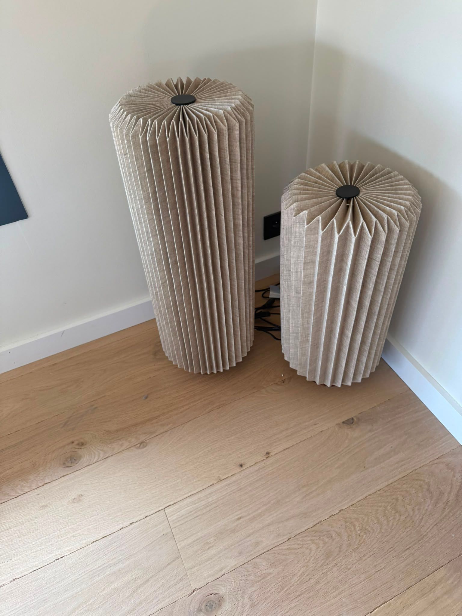 Deux poufs cylindriques côtelés beige dans un coin, sur un parquet clair