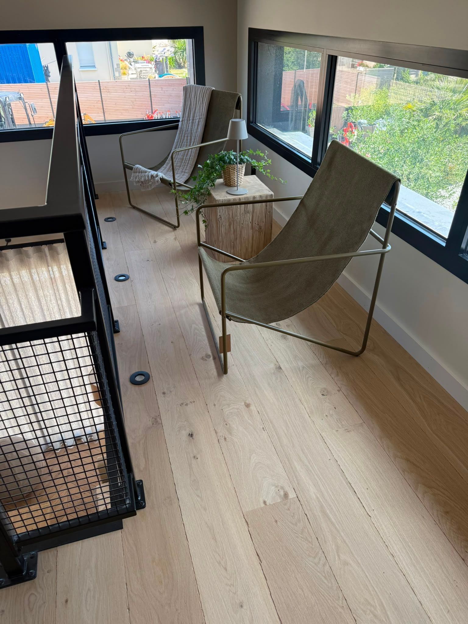 Deux chaises vertes sur un petit balcon, près de fenêtres, avec une table noire et une vue sur la ville en arrière-plan.