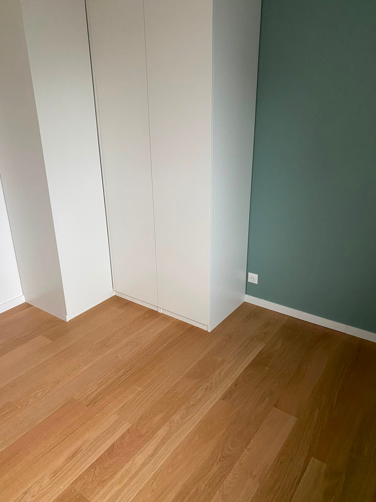 Coin de pièce vide avec des placards blancs, un mur vert et un parquet en bois.