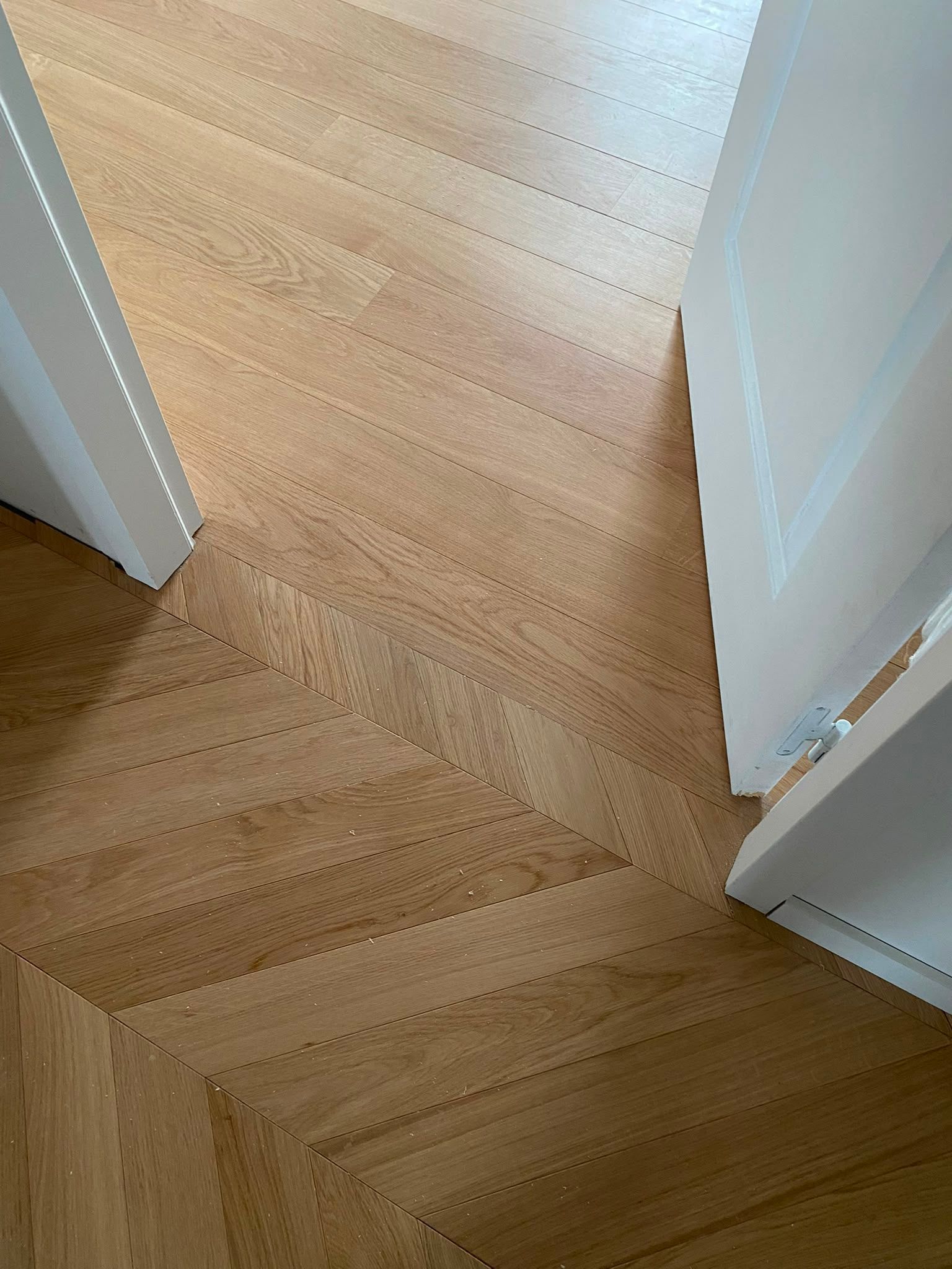 Parquet clair à chevrons entre deux portes blanches, vu du dessus