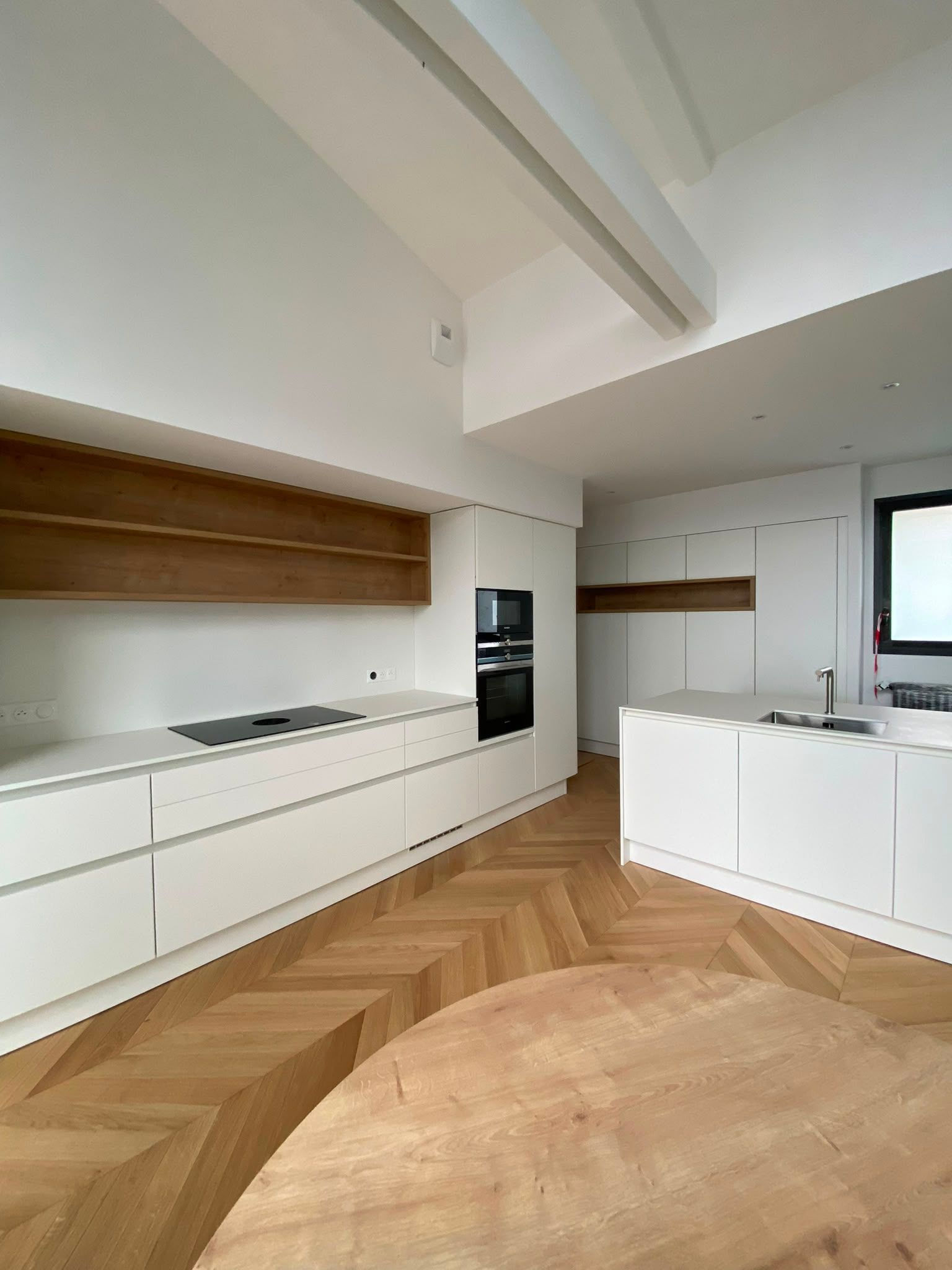 Cuisine moderne et minimaliste avec des placards blancs, des touches de bois et un parquet à chevrons