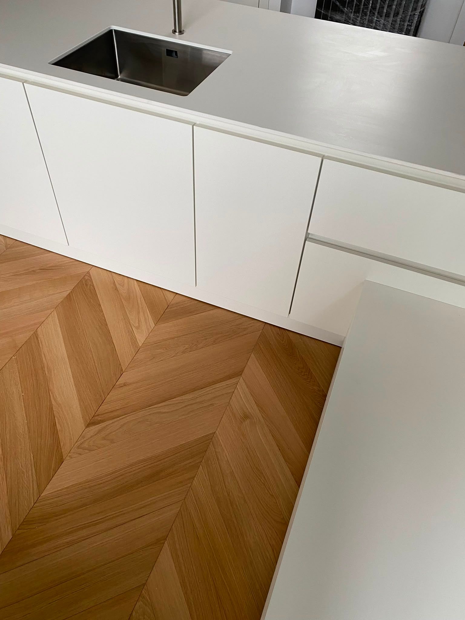 Cuisine moderne avec des placards blancs, un évier en inox et un parquet à chevrons