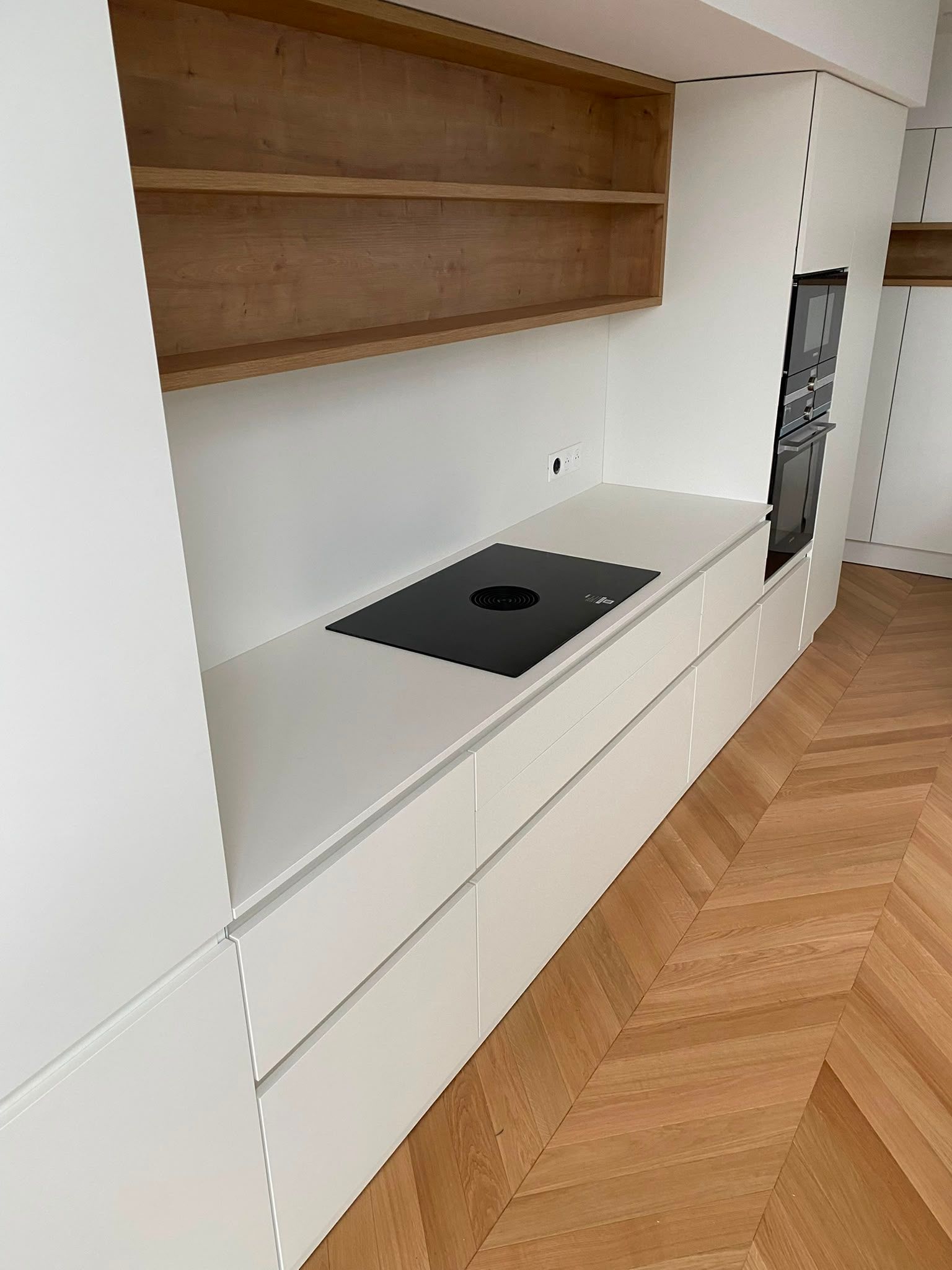 Cuisine blanche minimaliste avec plaque de cuisson intégrée, étagères en bois et parquet en chevrons