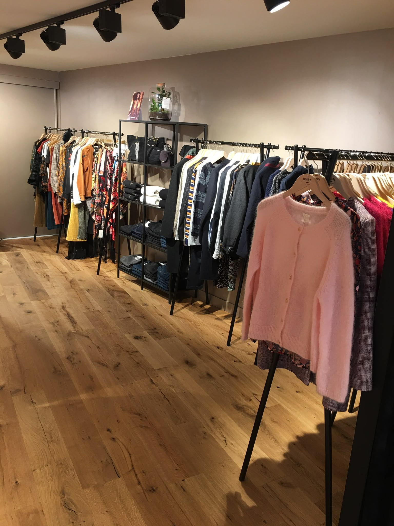 Intérieur d’un magasin de vêtements avec des portants garnis de vêtements variés, dont un pull rose au premier plan.