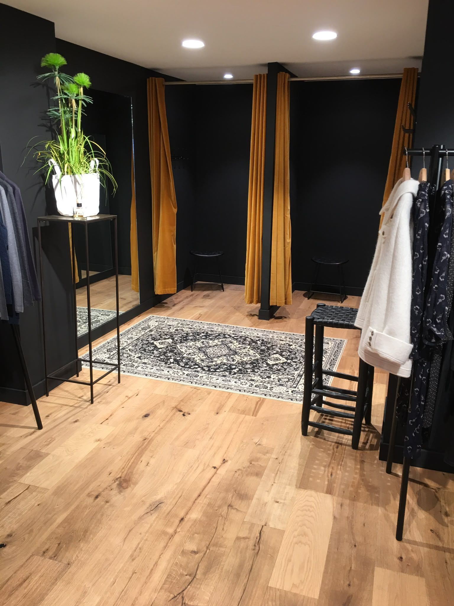 Intérieur d’une boutique de vêtements avec des portants, des rideaux de cabine d’essayage, un tapis et un parquet en bois.